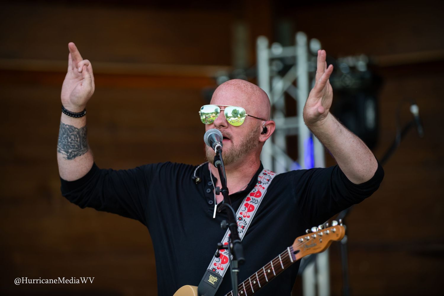 Energetic performer in dark clothing sings passionately into microphone on stage during live music performance.