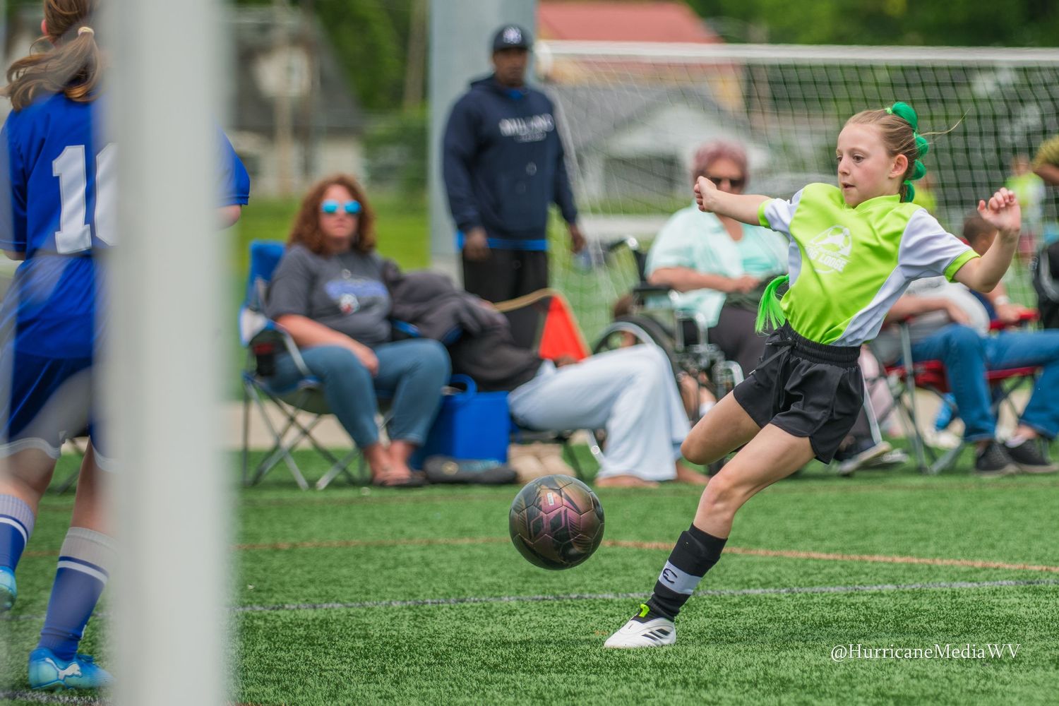 Soccer ball rolling on grass field during youth game with goal posts visible in background.