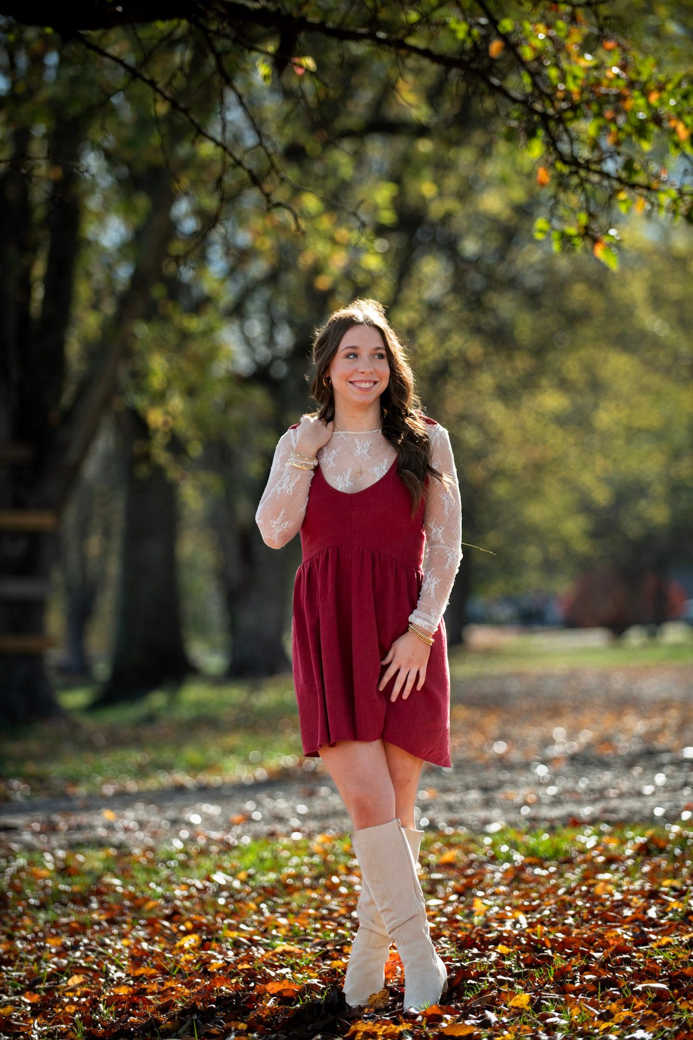 Figure in burgundy dress twirls playfully among fallen autumn leaves in park setting.