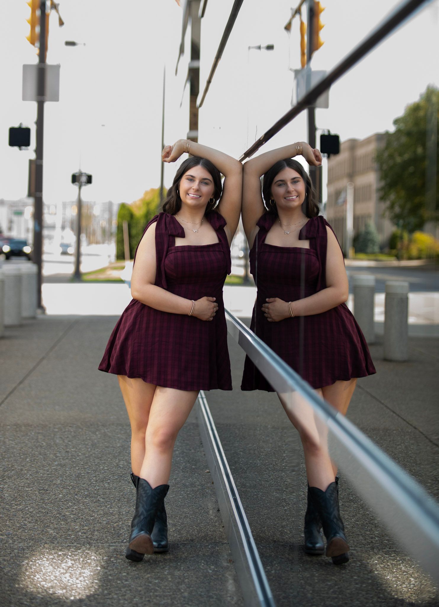 Two people in matching burgundy dresses pose creatively with a railing on an urban street.