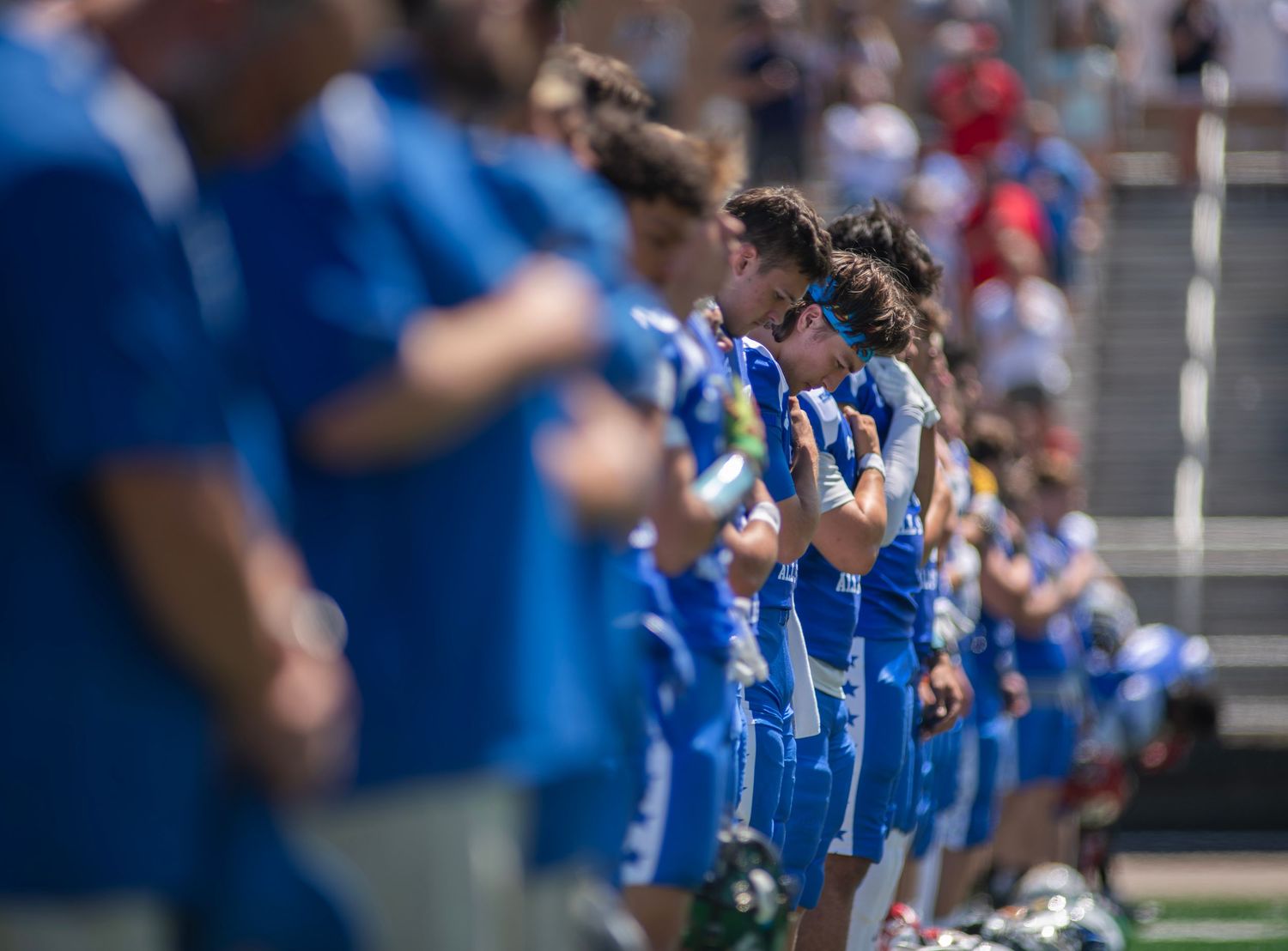 Soccer players in blue uniforms line up on a sunny field during a pre-game ceremony.