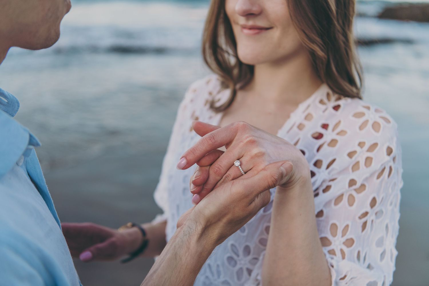 Close up of engaged couple holding hands while showing off diamond engagement ring on beach.