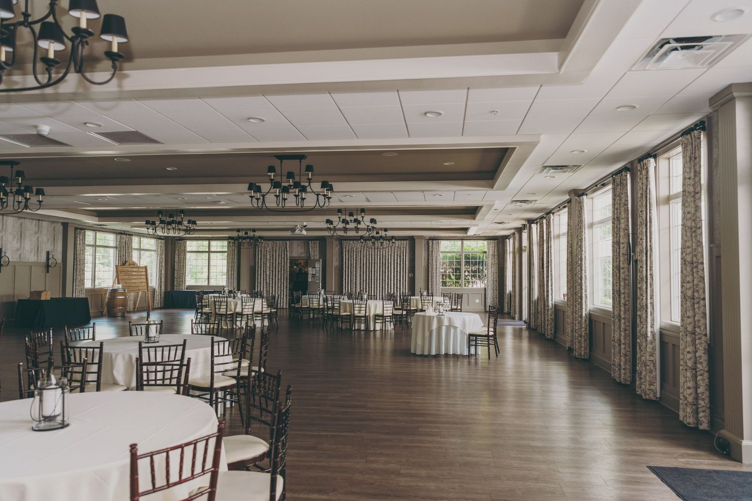 Elegant ballroom with wooden floors, chandeliers and large windows set up for a wedding reception.