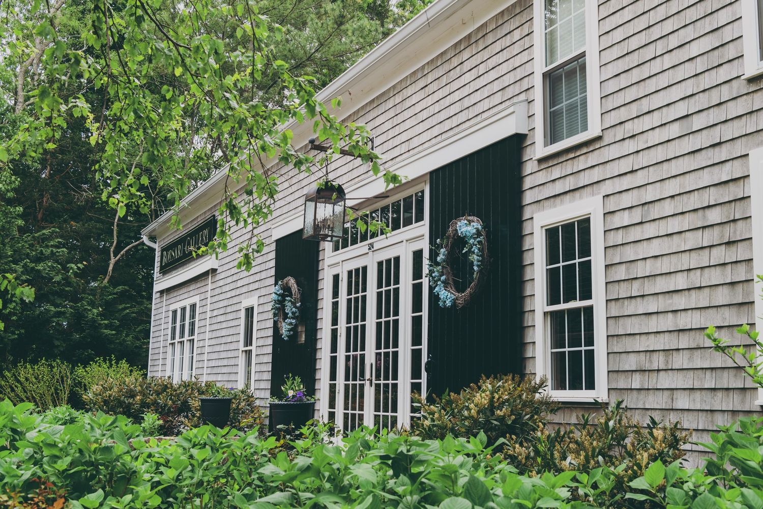 A series of weathered gray cedar shingle siding panels on a classic New England style house with white trim and windows.