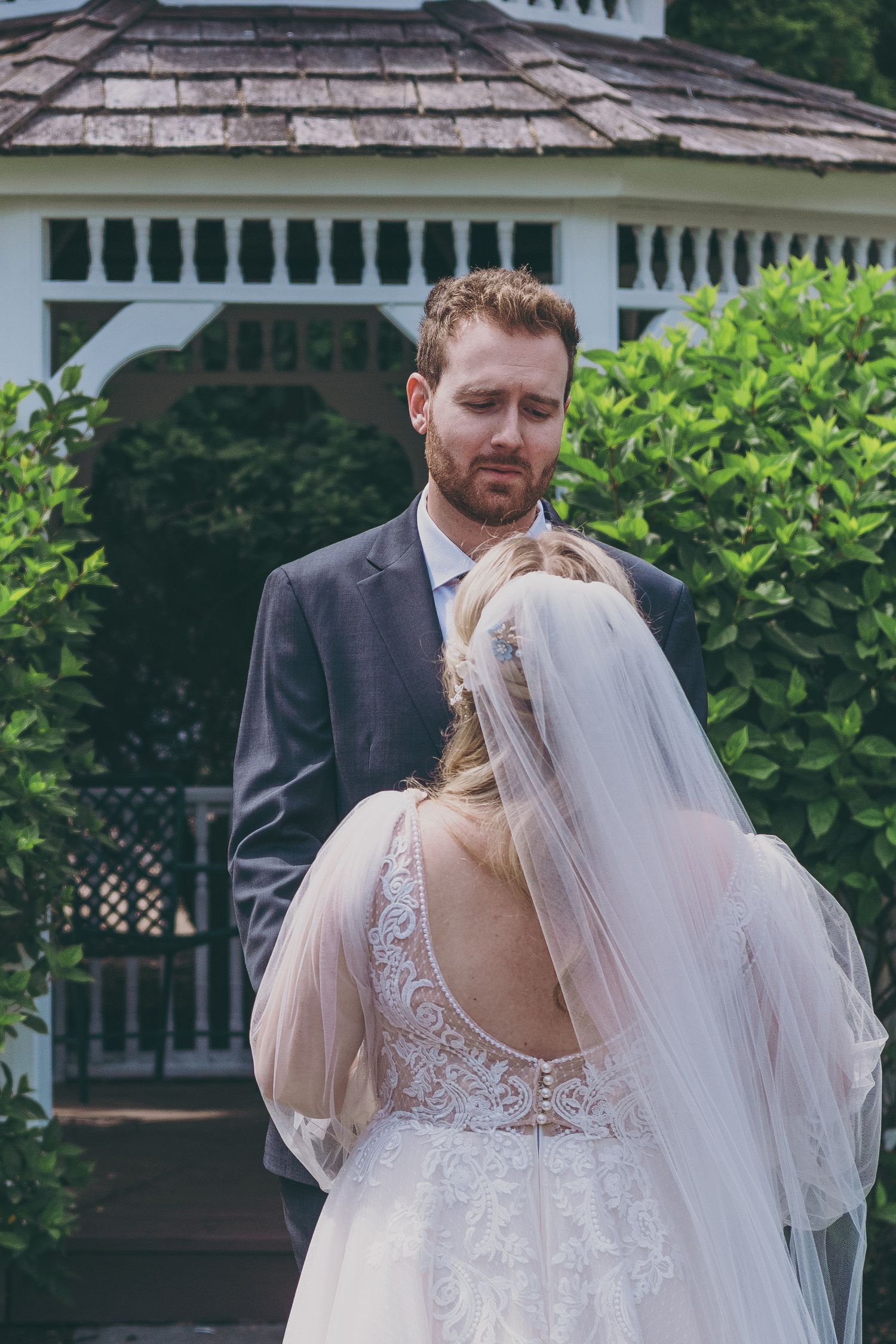 A romantic outdoor wedding scene with a white dress and black suit against a gazebo and garden background.