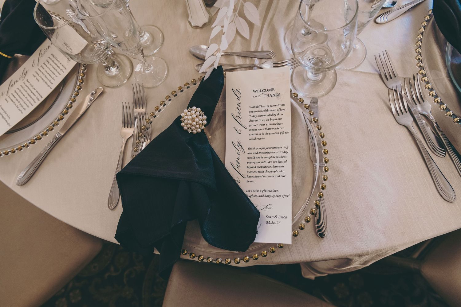 Elegant table setting with silver cutlery and menu cards arranged on white linens against dark green accents.