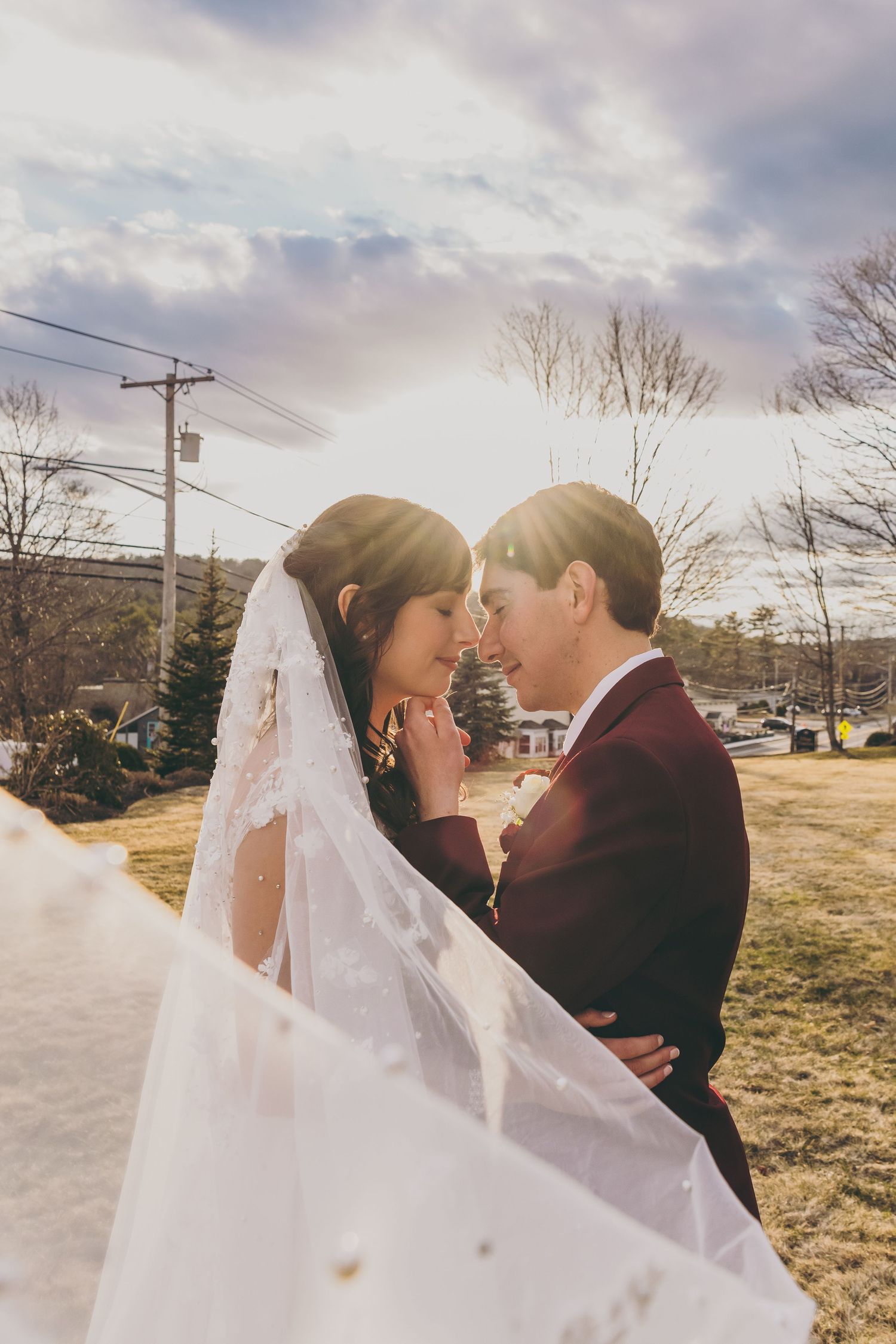 Romantic sunset wedding portrait with couple sharing intimate moment as veil flows in the wind.