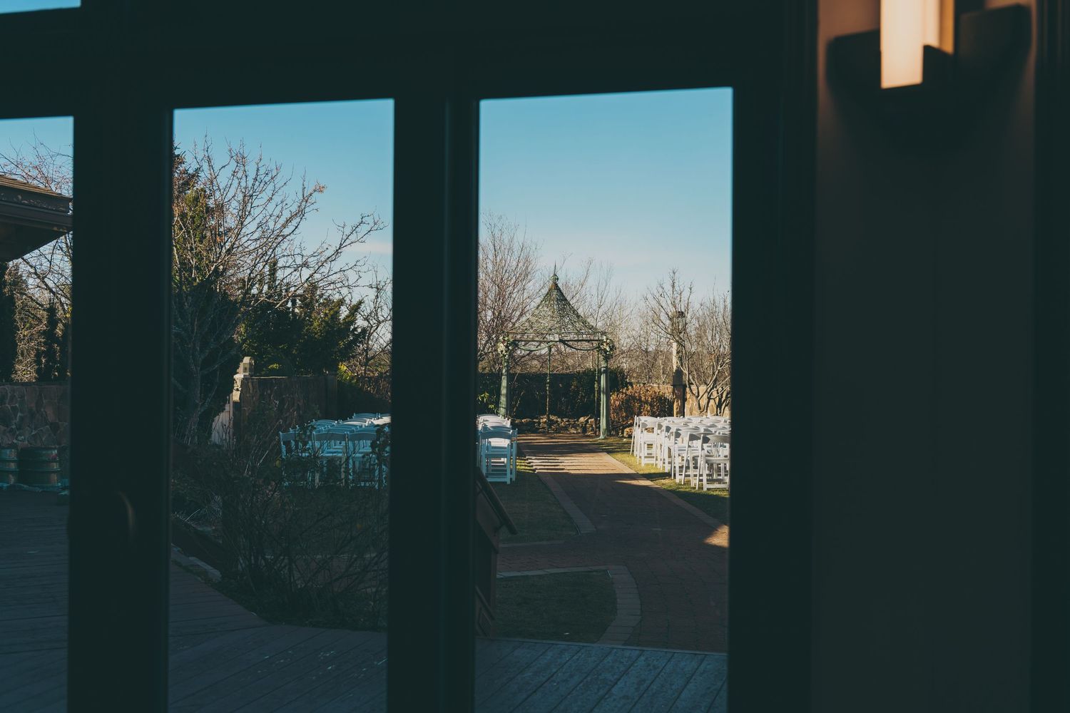 View through dark framed windows of an outdoor wedding venue with bare winter trees in the distance.