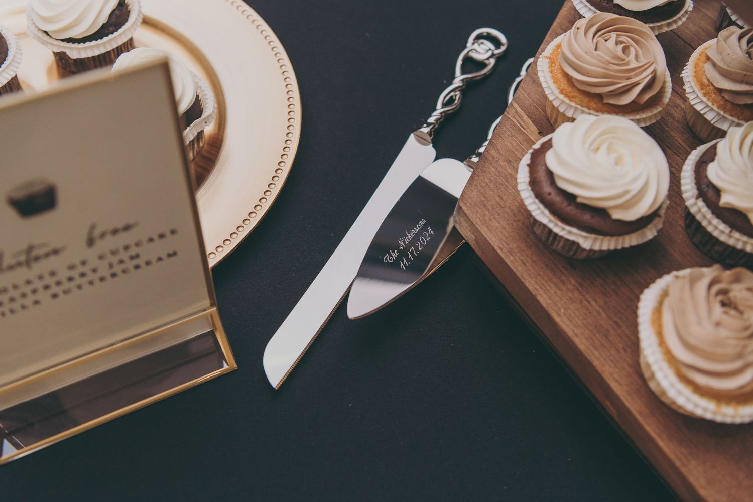 Wedding cake server and cupcakes with frosting on wooden serving board.
