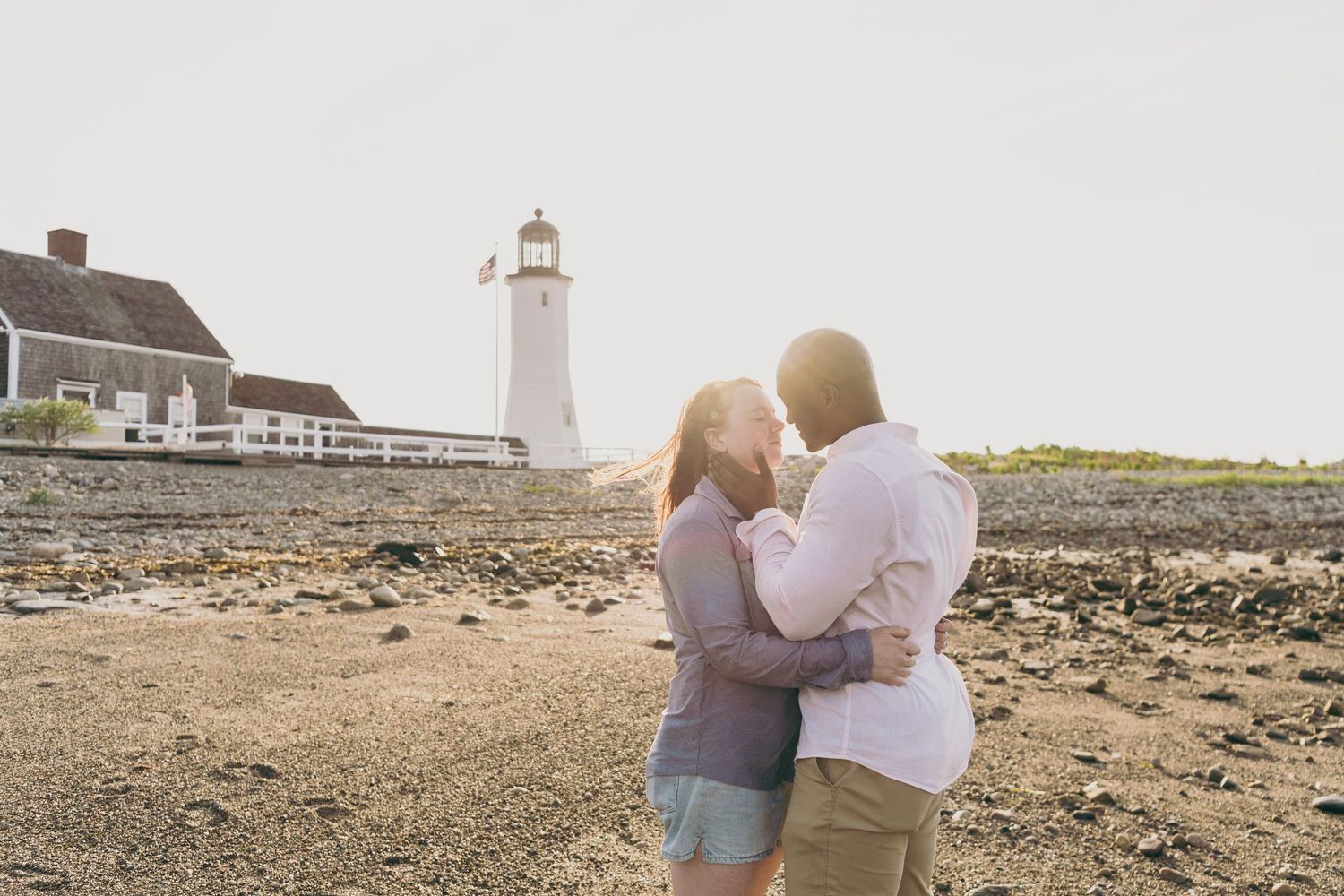 A romantic moment captured by a lighthouse on a rocky beach during golden hour.