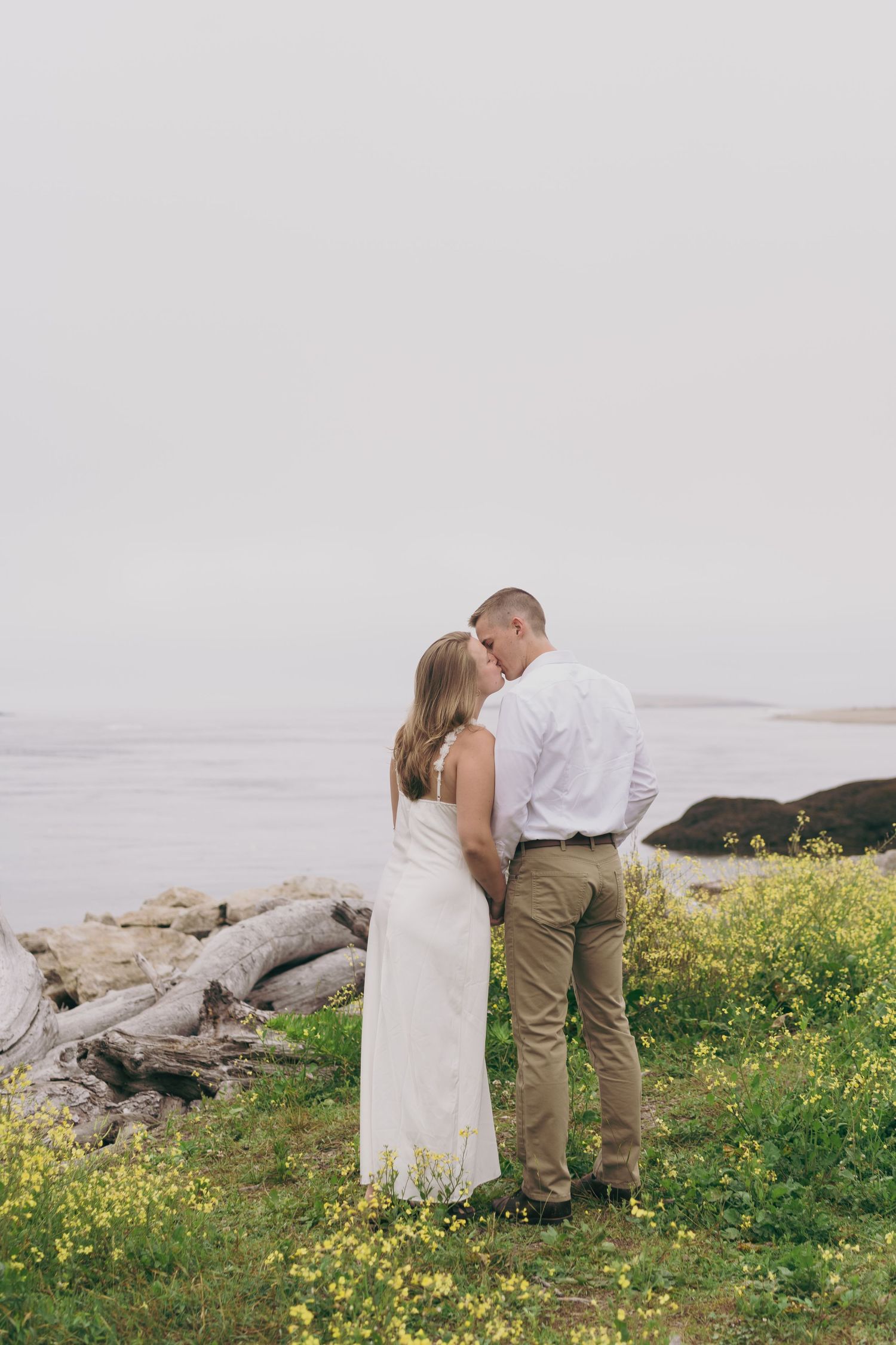 A romantic series of photos showing a couple in white and khaki sharing tender moments by coastal rocks and wildflowers.
