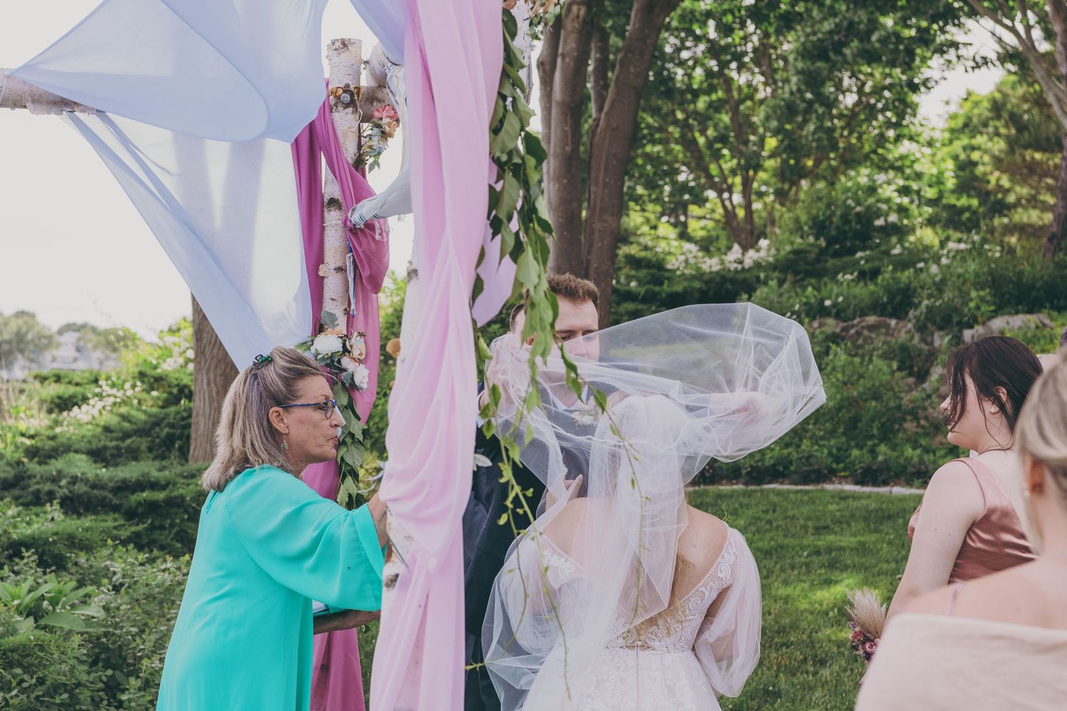 Wedding ceremony with pink and white fabric decorations in outdoor garden setting.