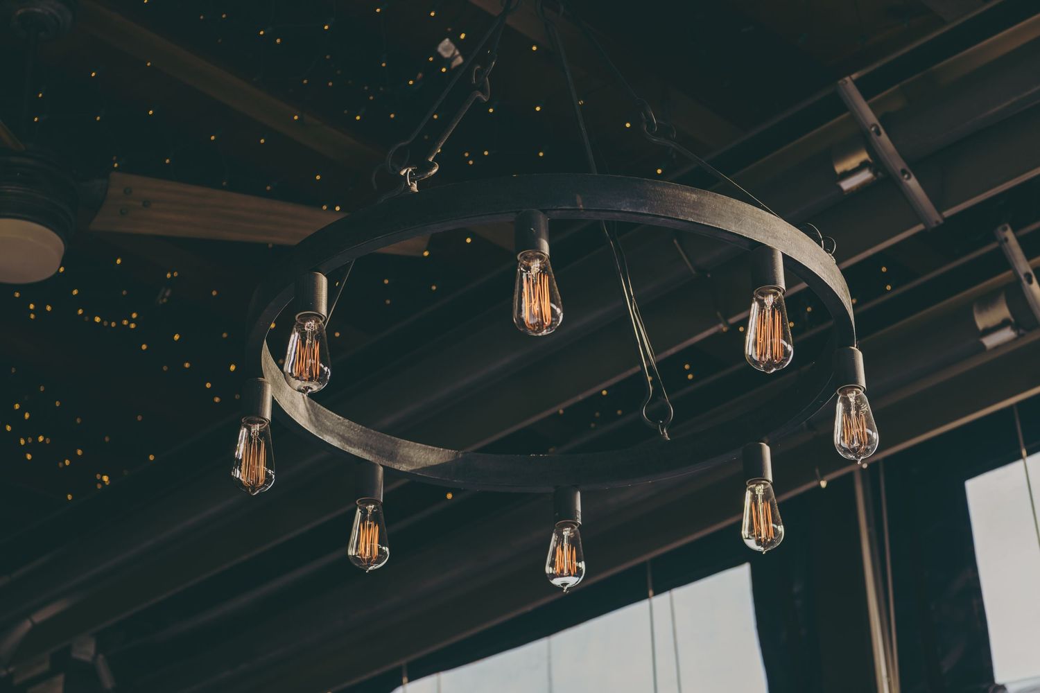 A curved industrial light fixture with exposed Edison bulbs hangs from a dark ceiling with twinkling lights.