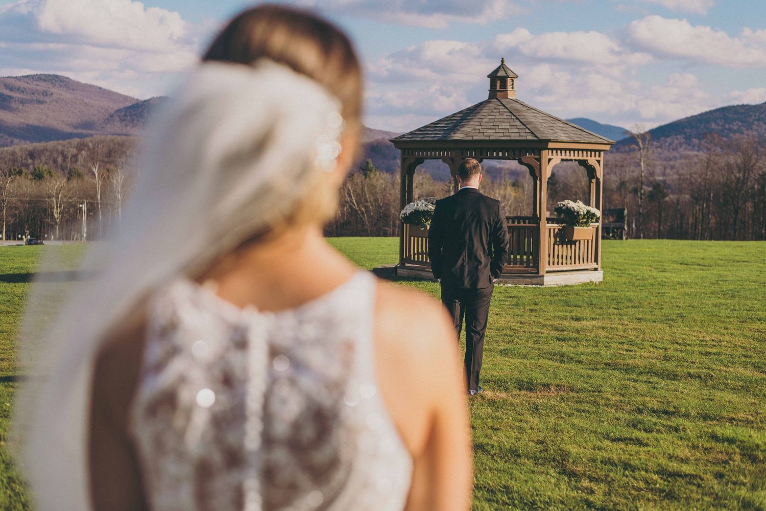 A couple walks towards a wooden gazebo in a scenic mountain landscape on their wedding day.