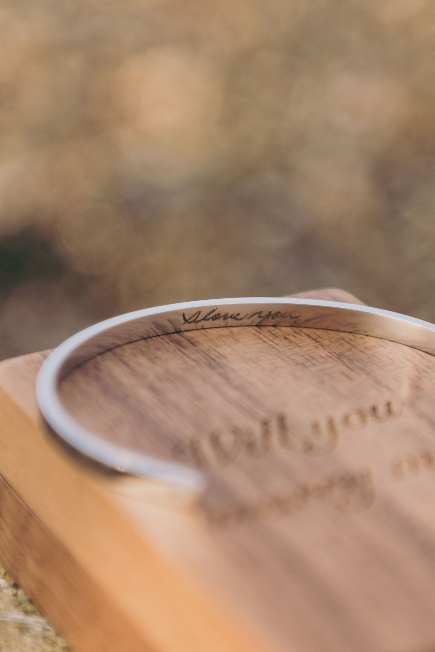 Close-up view of a silver engraved ring on a wooden surface with blurred background.