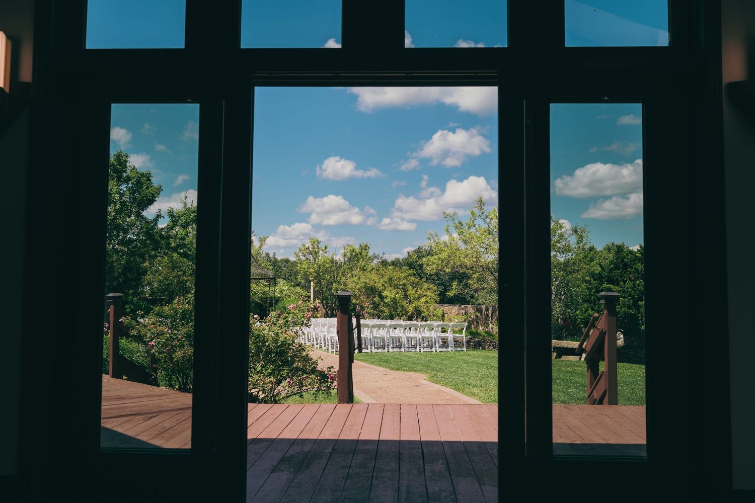 View through wooden doorframe of sunny wooden deck and lush green landscape with puffy white clouds in blue sky at the Granite Rose.