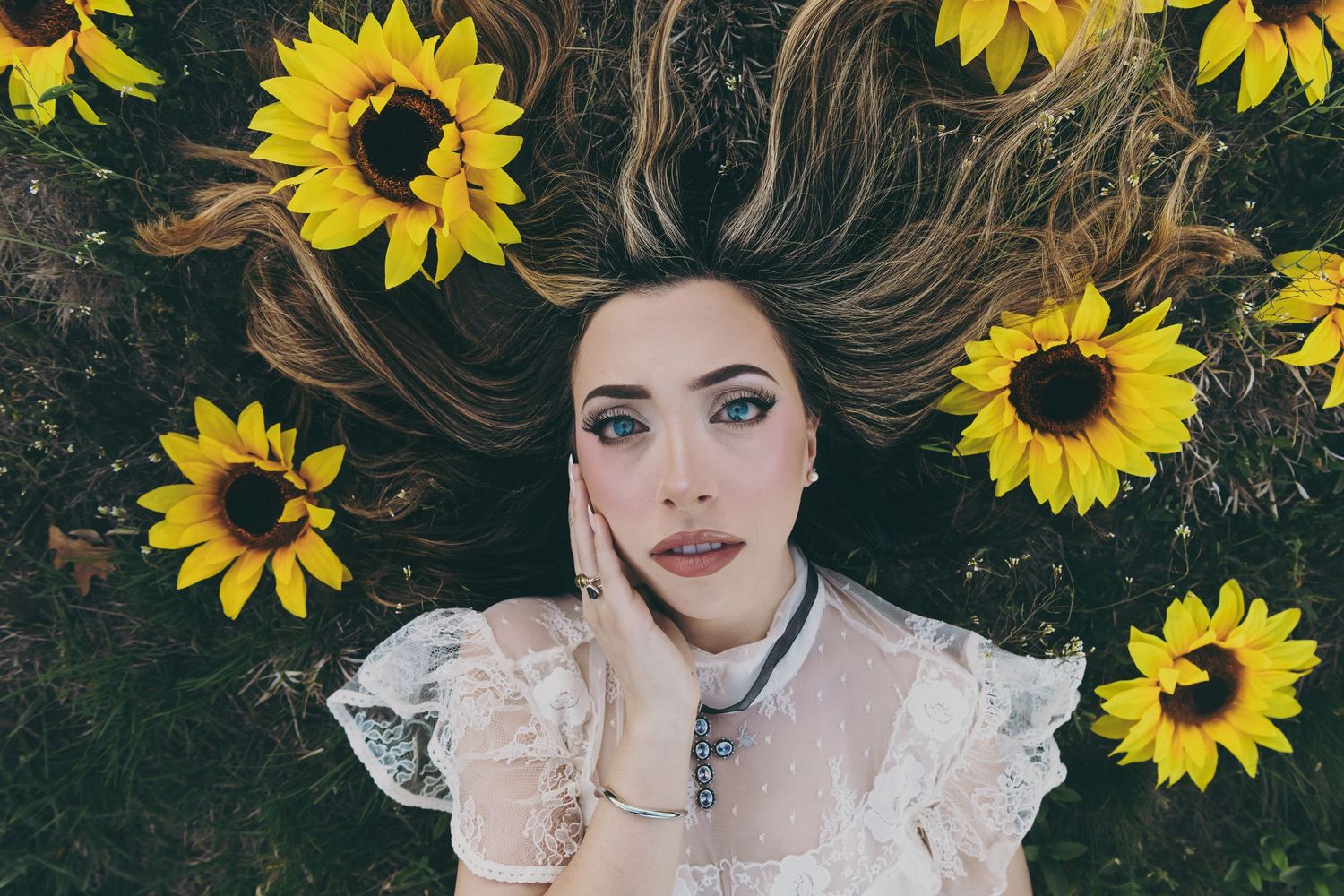 Artistic portrait surrounded by bright yellow sunflowers on dark grass background.
