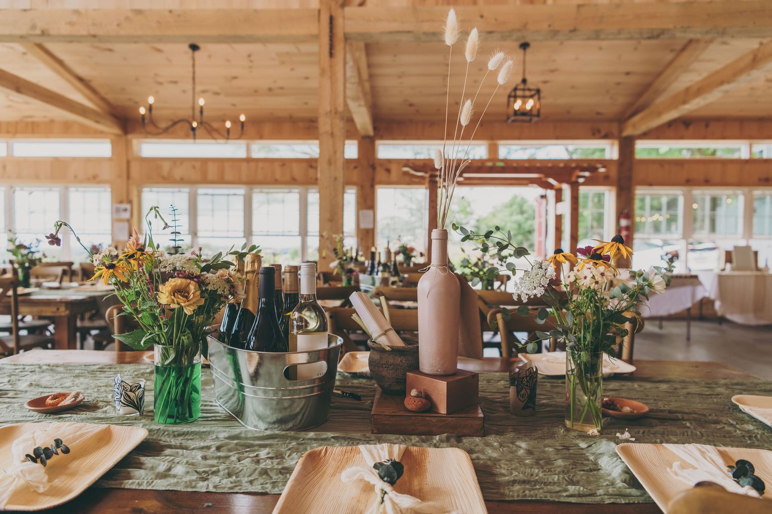 Rustic wedding reception venue with wooden beams, sunflowers in vases, and elegant table settings inside a barn-style space.