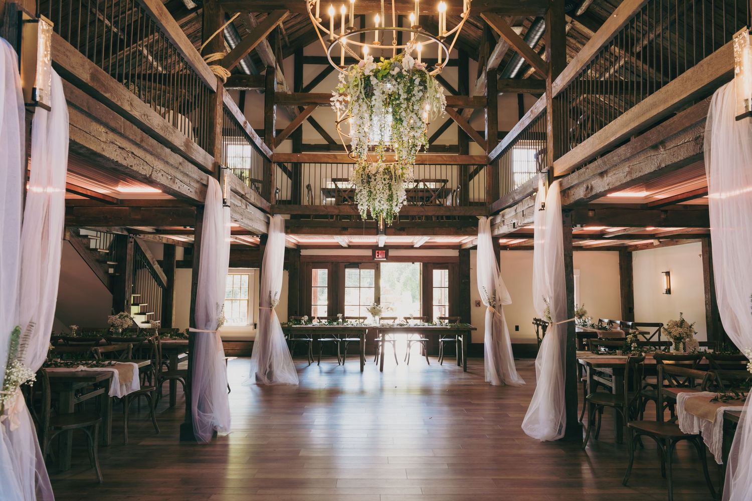 Elegant rustic barn venue interior with chandelier, wooden beams and white drapes for a wedding reception.