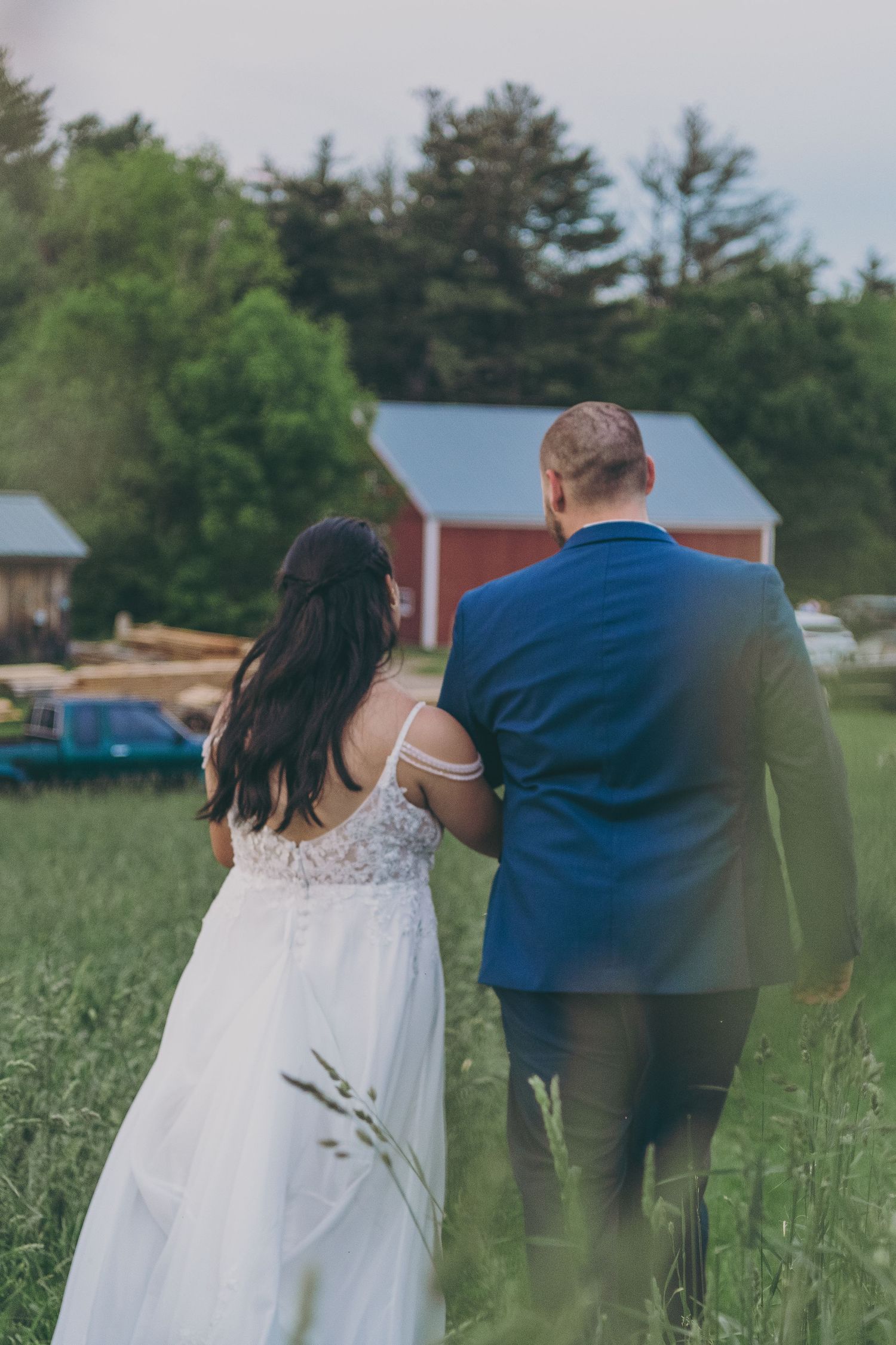 Wedding couple walking through a rustic field with red barn in background.