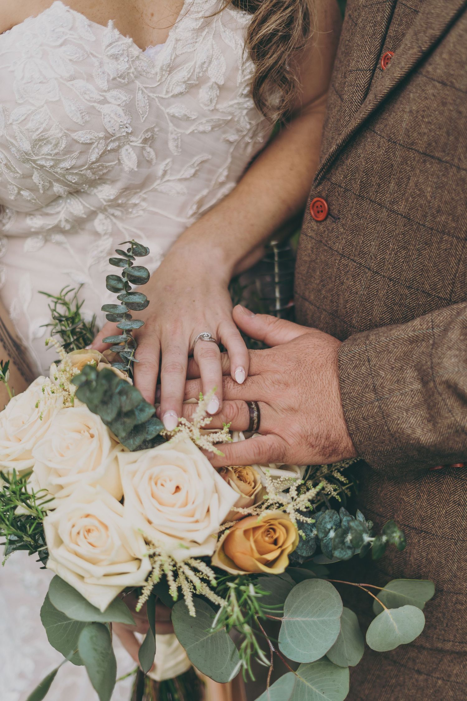 Close up of hands holding a romantic bridal bouquet with white roses, eucalyptus, and greenery.