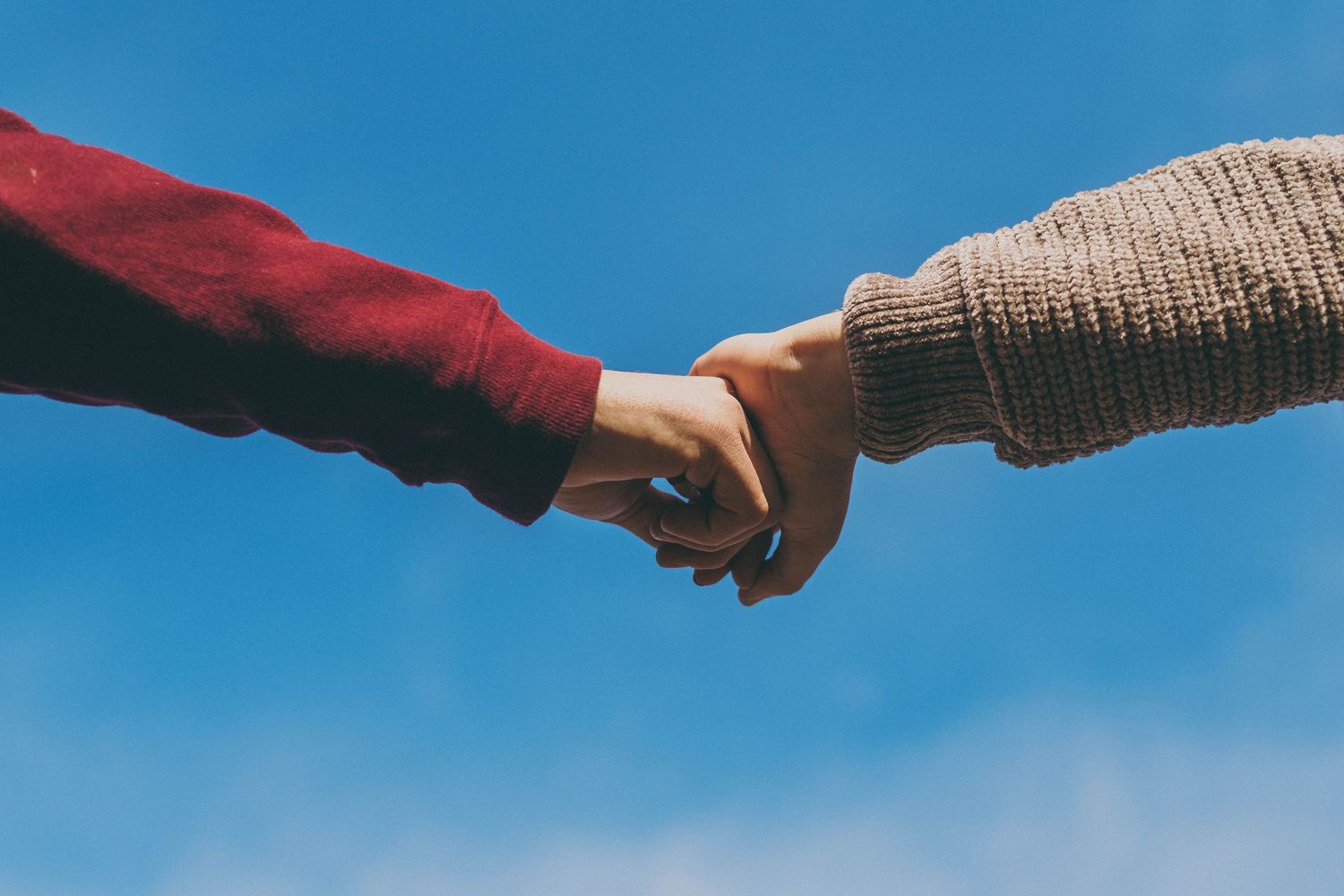 Hands reaching across against a bright blue sky creating a silhouette effect.