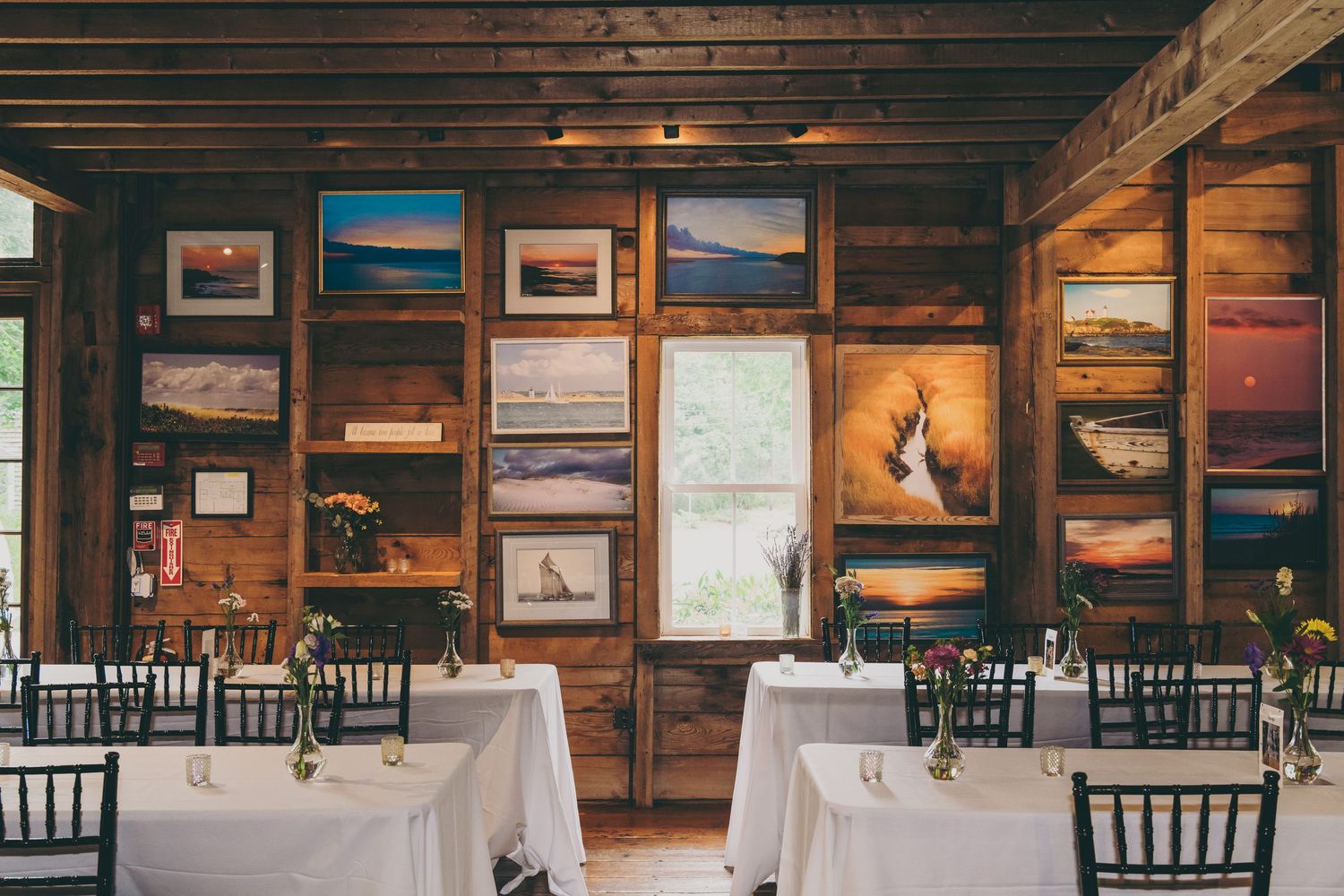 Rustic wedding reception venue with wooden walls decorated with landscape photographs and white tablecloths.