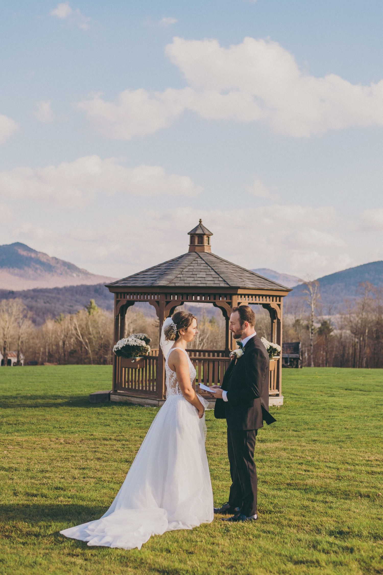 A couple shares their first look moment in a scenic mountain field with a wooden gazebo in the background.