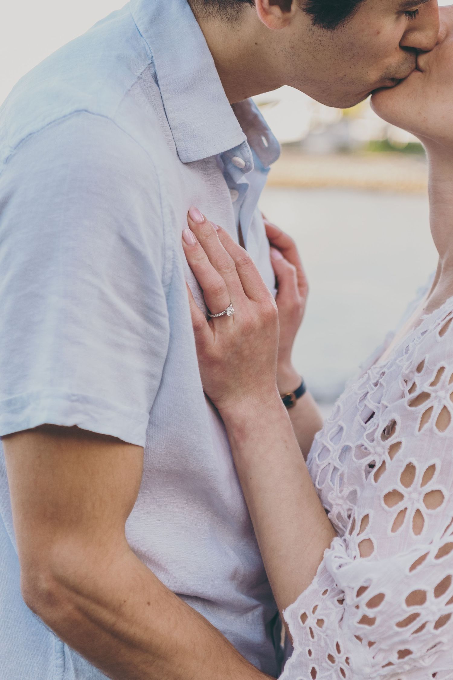 Close up of a romantic kiss with delicate lace dress details and a prominent engagement ring on display.