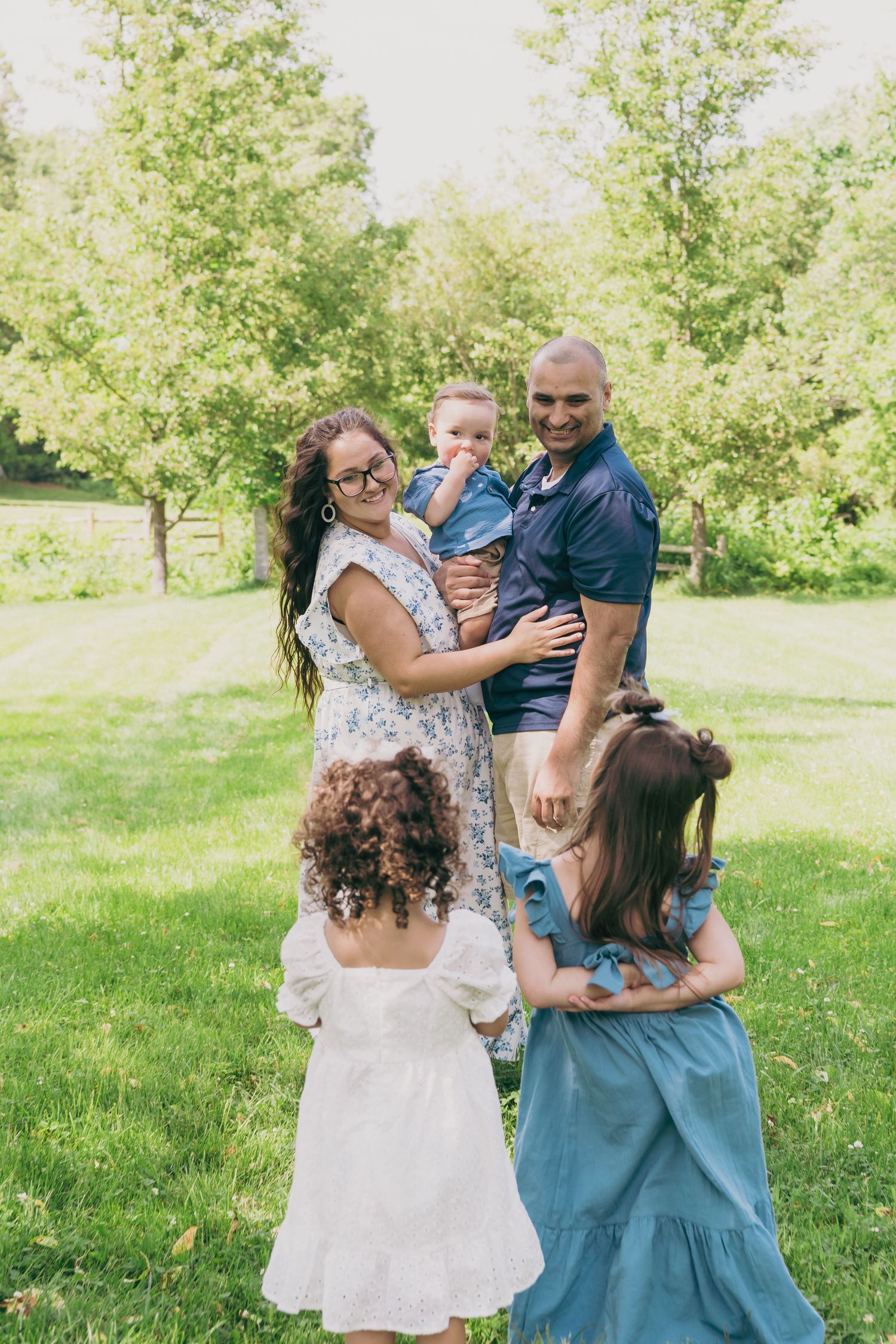 A family poses together on a grassy lawn with trees in the background.