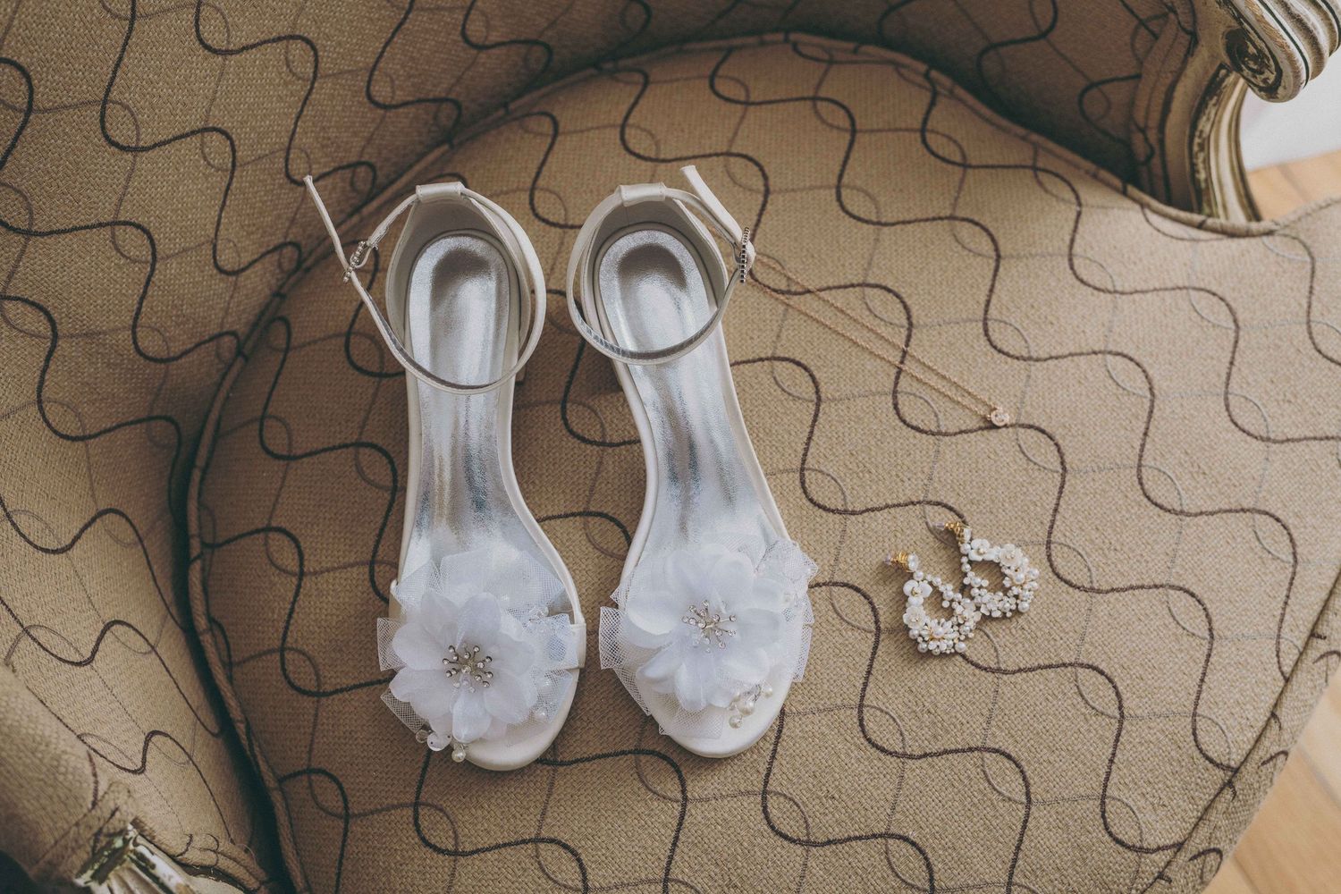 Elegant white bridal sandals with floral details rest on a wavy textured beige carpet.