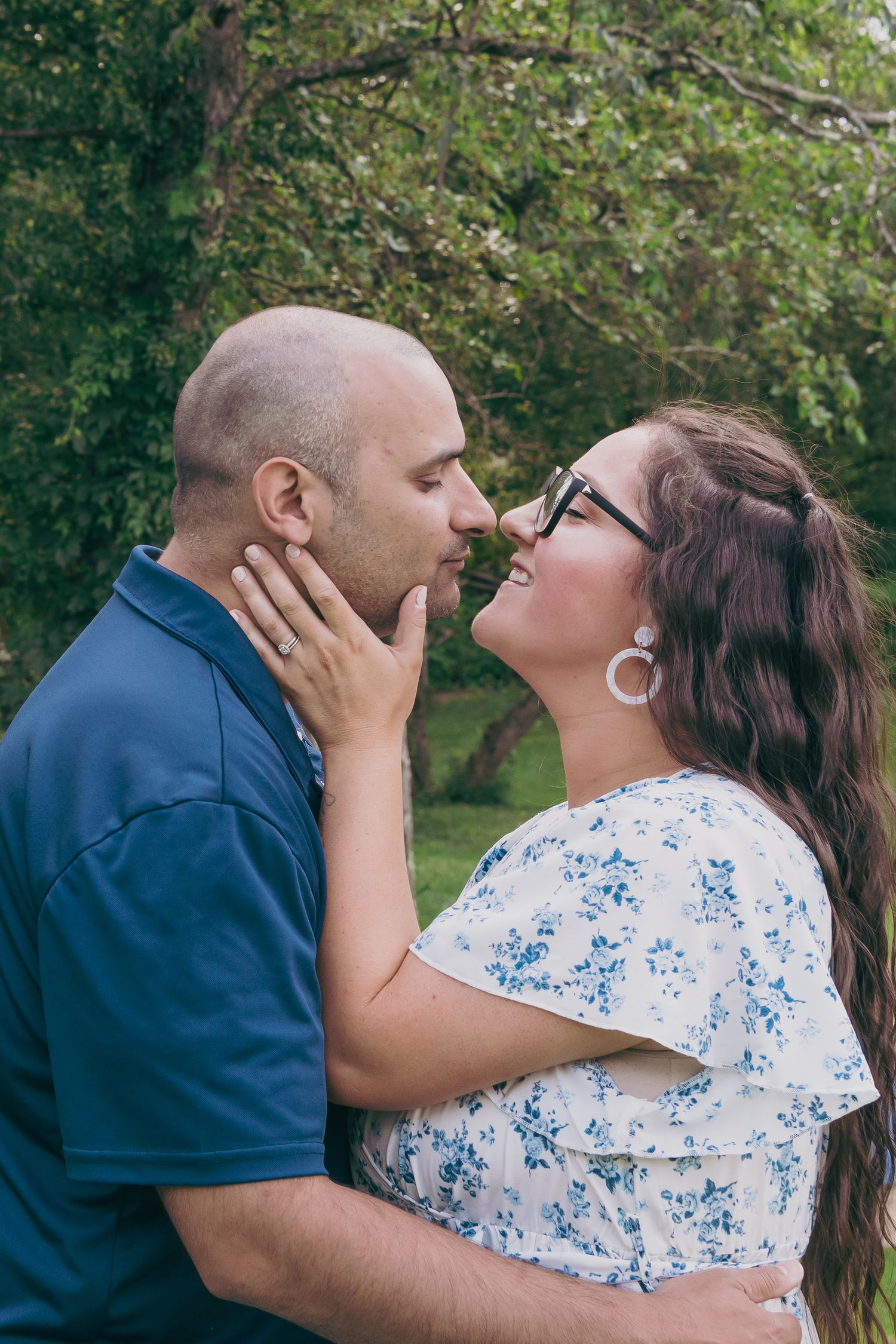 A romantic moment between a couple in casual attire standing in a lush green park.
