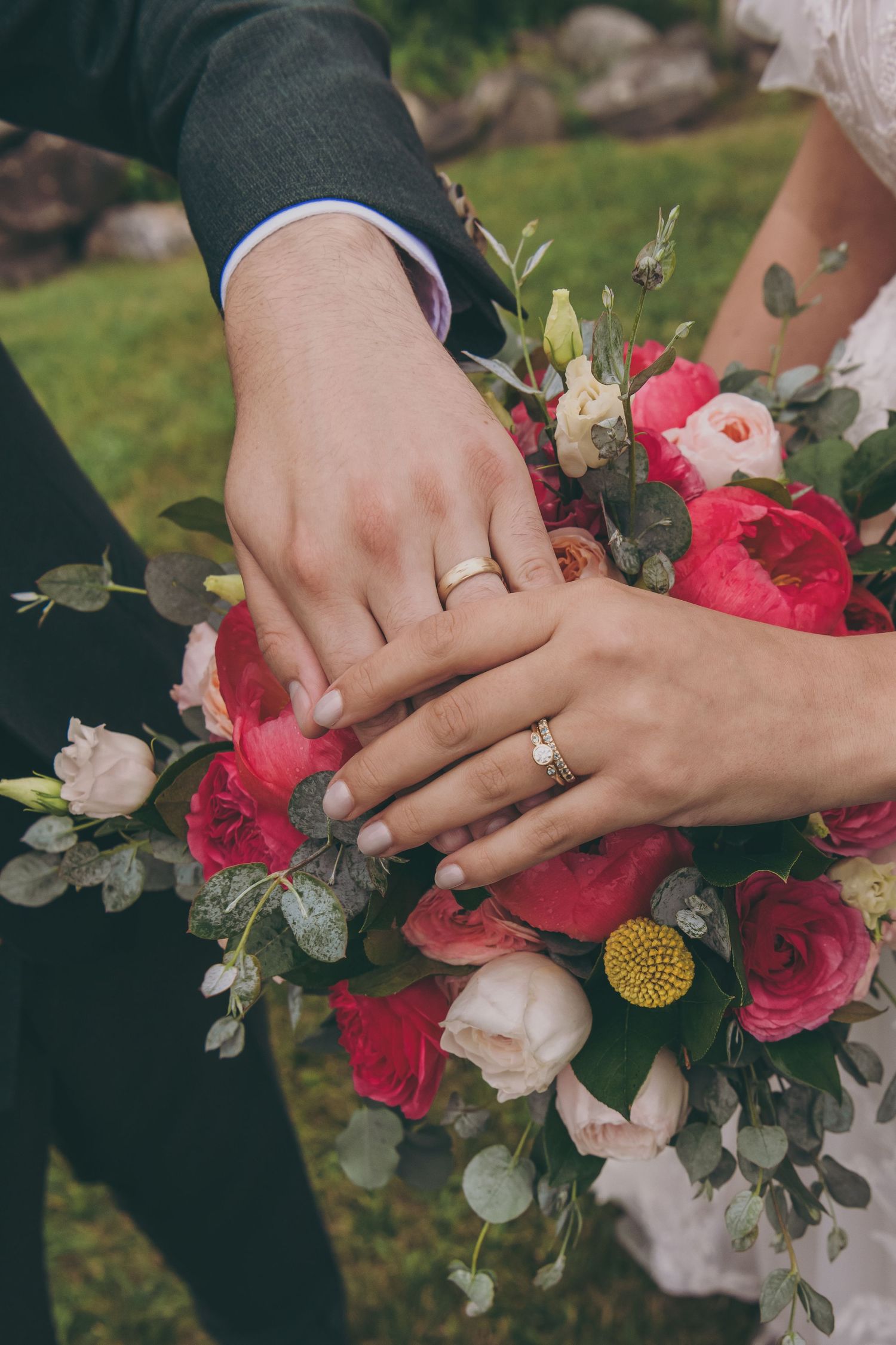 Close-up of wedding rings and hands holding beautiful pink and white floral bouquet.