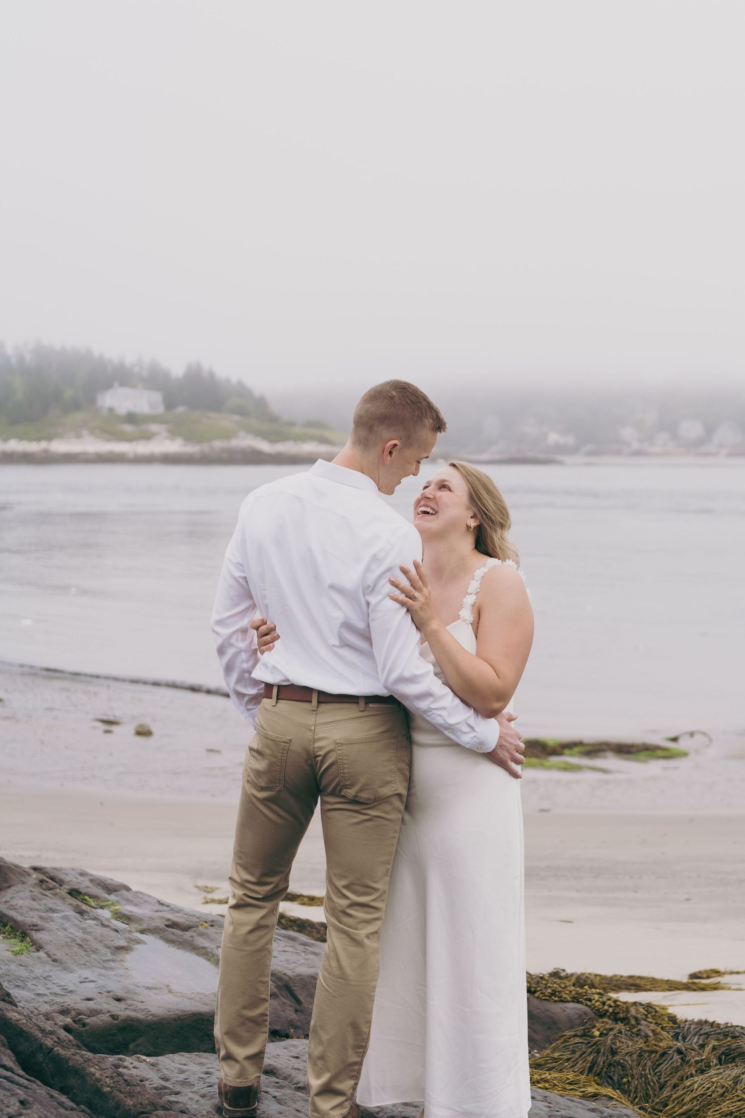 A couple shares a joyful moment together on a foggy rocky beach along the coast.