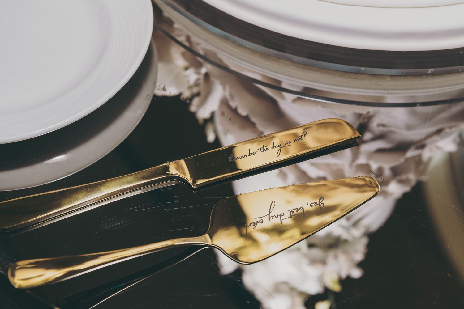 Gold engraved serving utensils with elegant handles laid on a dark surface next to white dinnerware.