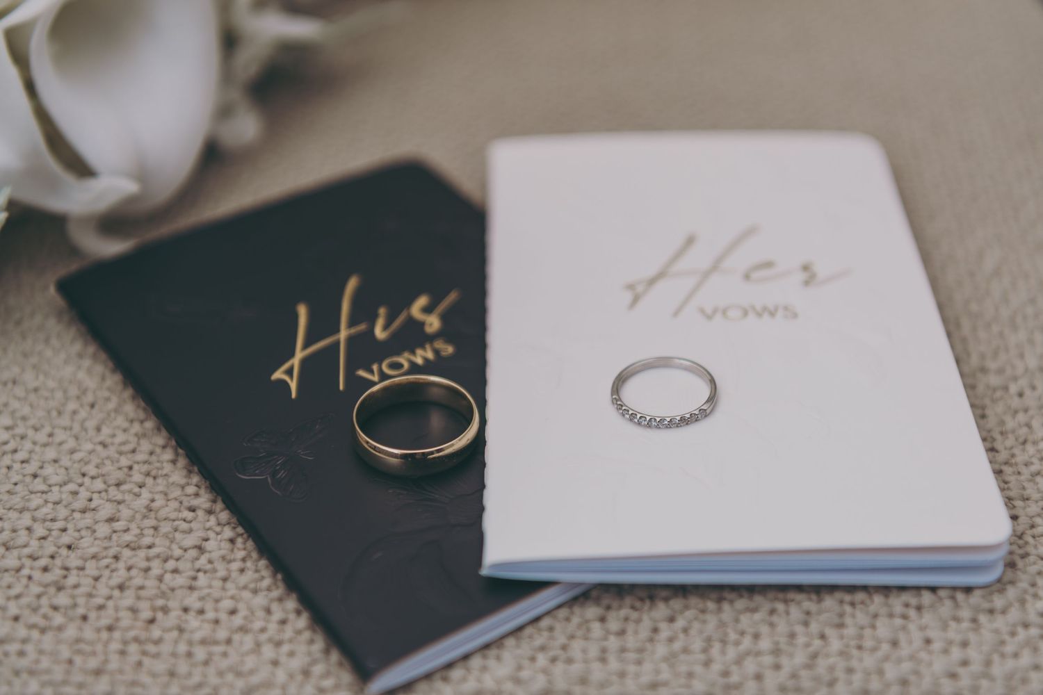 Wedding rings and vow books rest elegantly on a textured cream background.