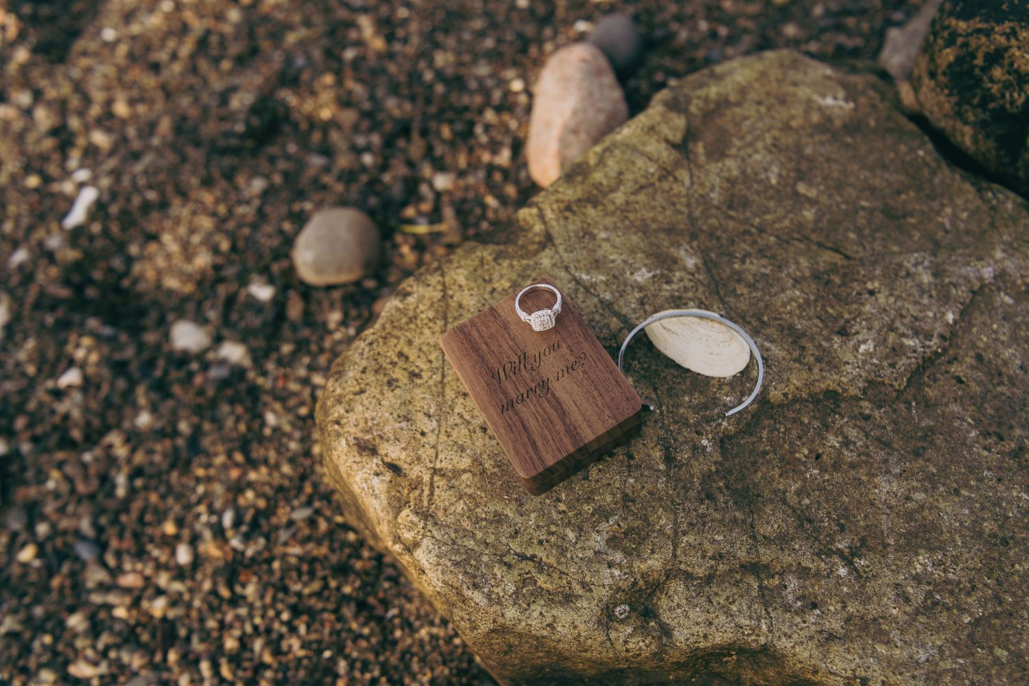Wedding rings and wooden box sitting on a large rock by the shore.
