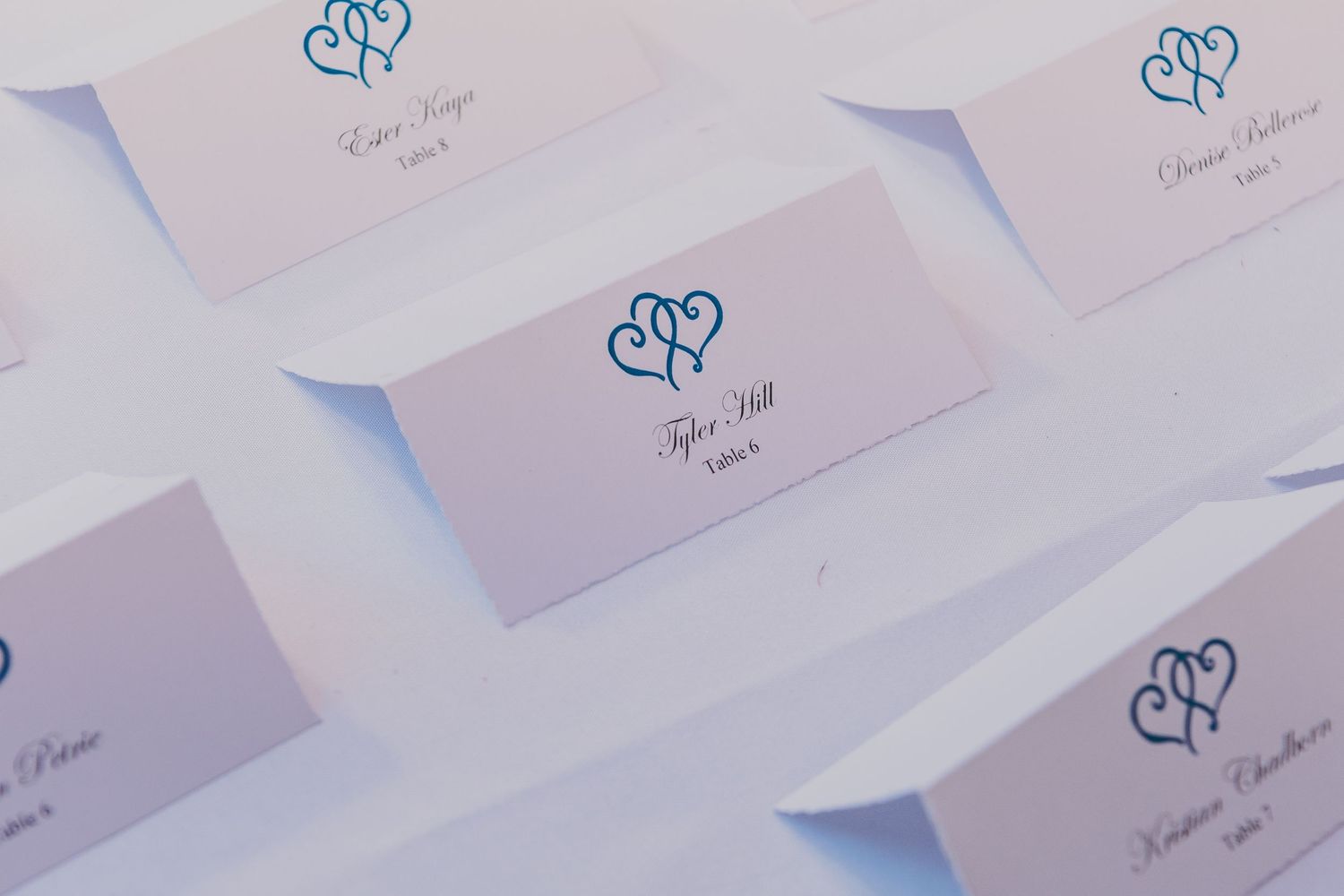 Elegant wedding place cards with double heart design stand in precise rows on white surface with purple lighting.