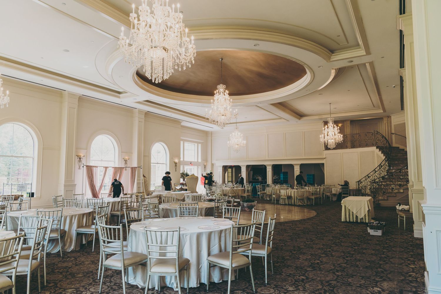 Elegant ballroom with crystal chandeliers, round white tables, and teal accent chairs in a classic wedding venue setting.