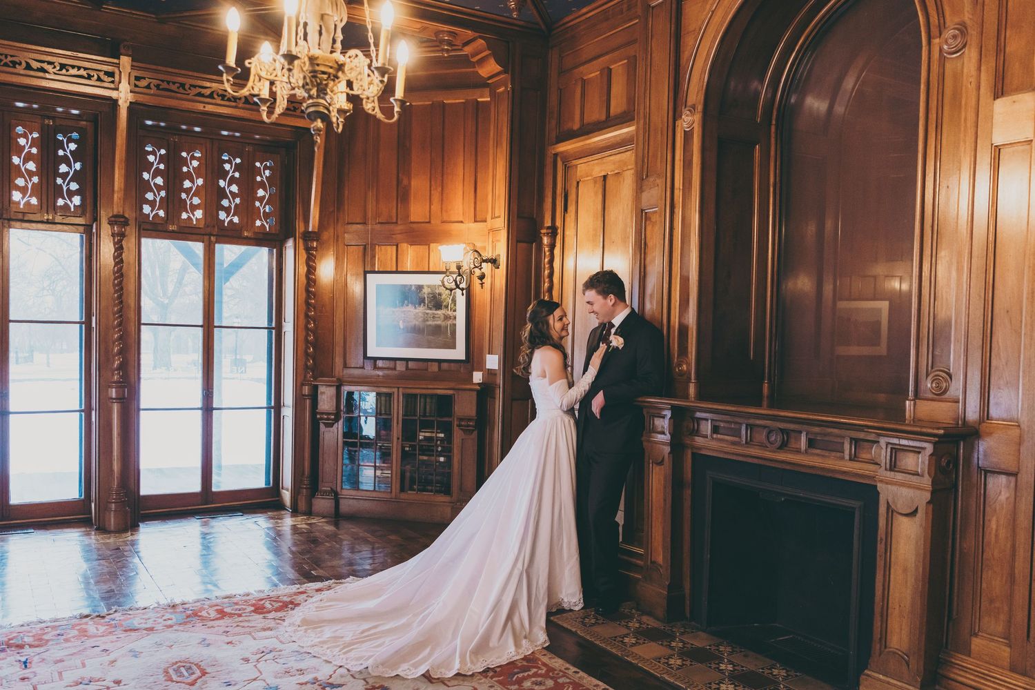 Grand Victorian ballroom with rich wood paneling, chandeliers and long flowing white fabric against windows.