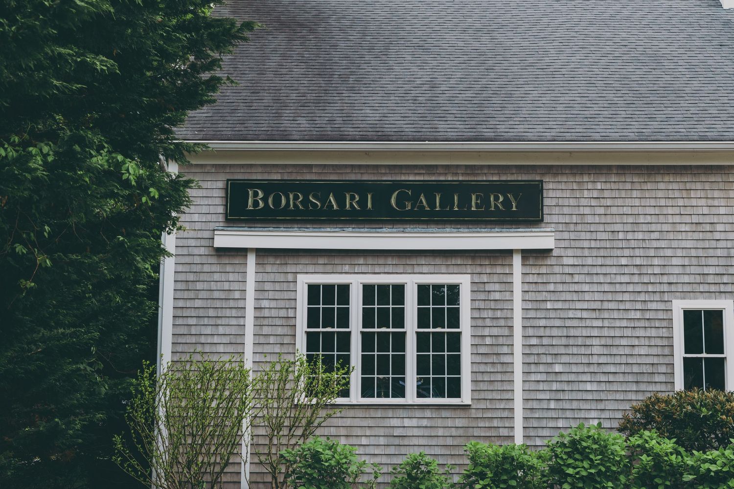 A gray shingled building exterior with a sign reading 'Bowsart Gallery' above white-framed windows.