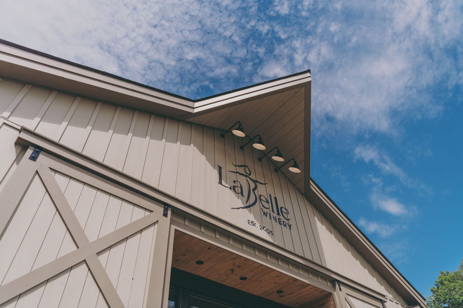White barn-style wedding venue exterior with rustic details against blue sky with wispy clouds.