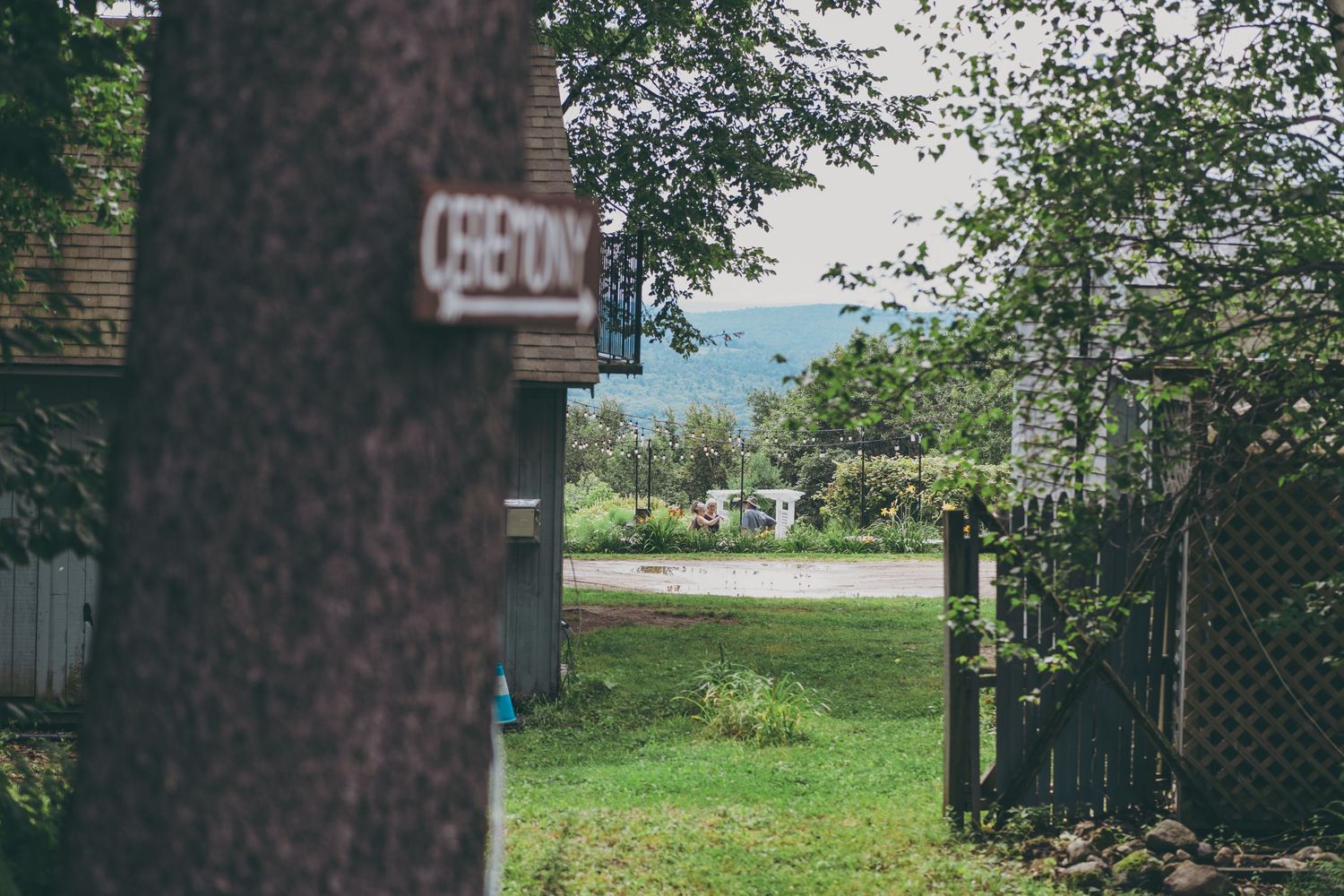 A narrow view through trees shows a house number marker and glimpse of a grassy yard on a sunny day.