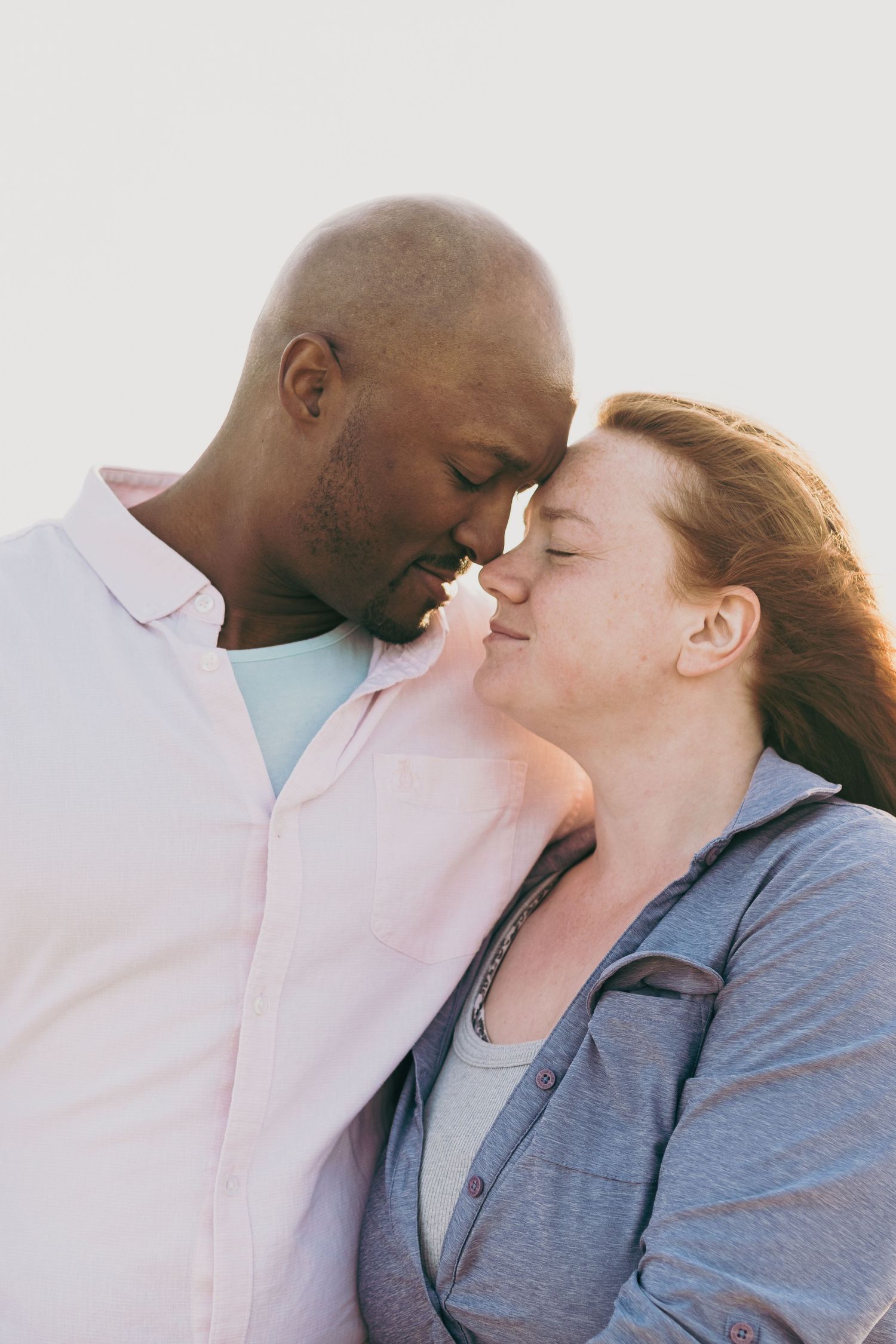 A romantic couple sharing an intimate moment together as they touch foreheads in soft lighting.