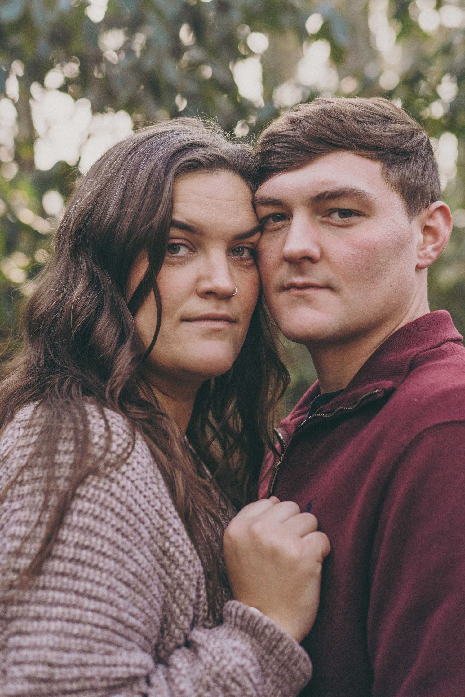 A romantic outdoor portrait of a couple in casual sweaters with soft bokeh background.
