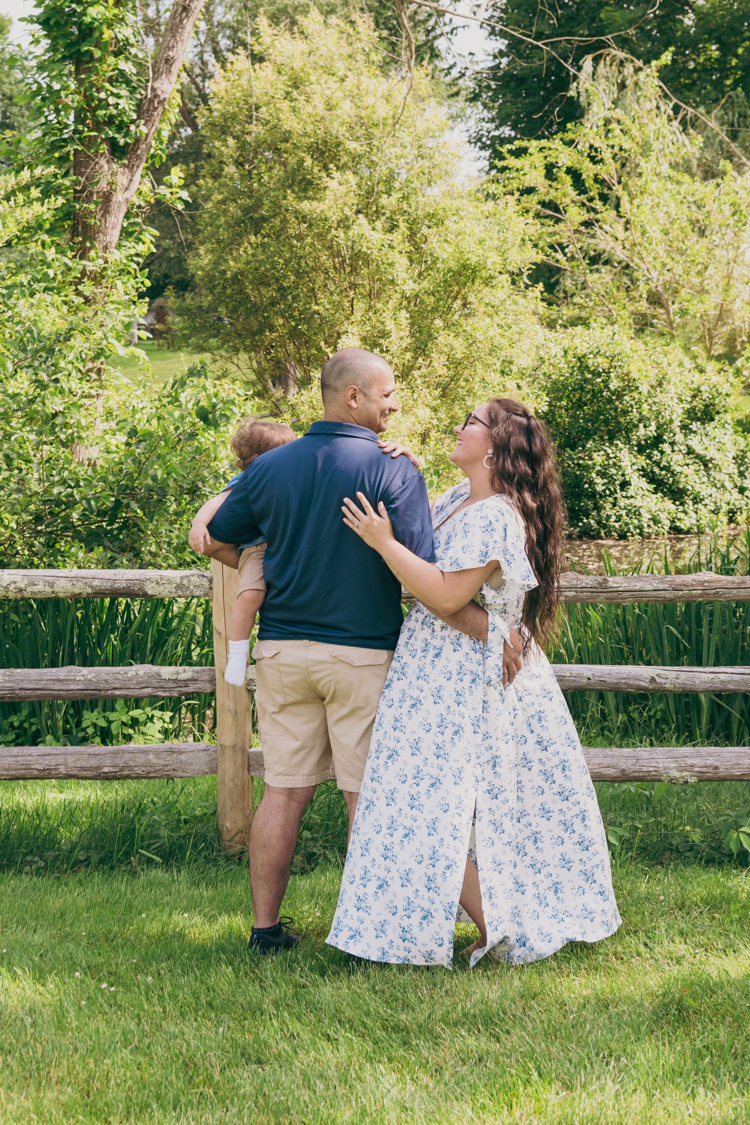 A couple stands together against a wooden fence overlooking a serene natural landscape.