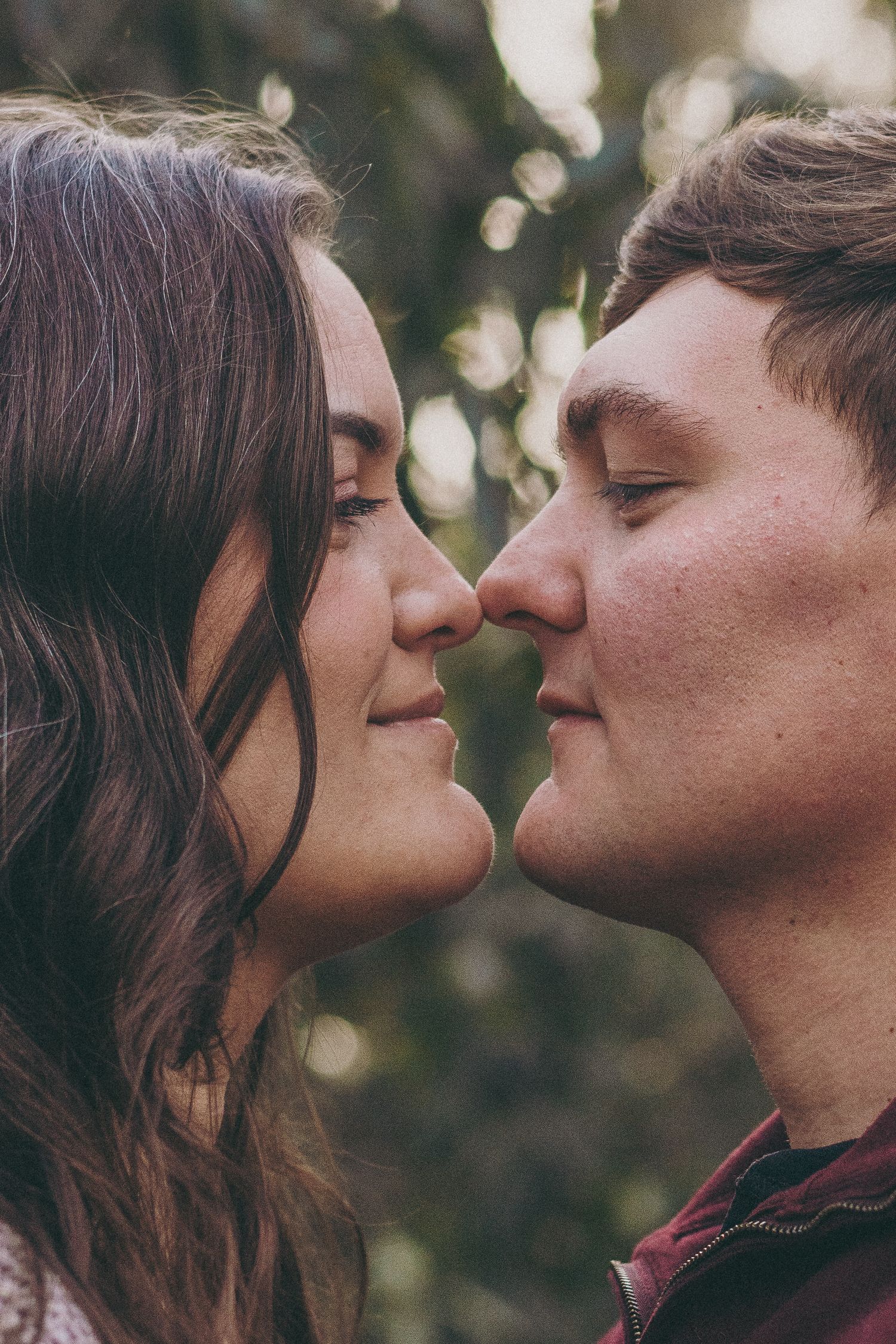 Intimate couple in a close embrace outdoors with soft natural lighting and bokeh effect in background.