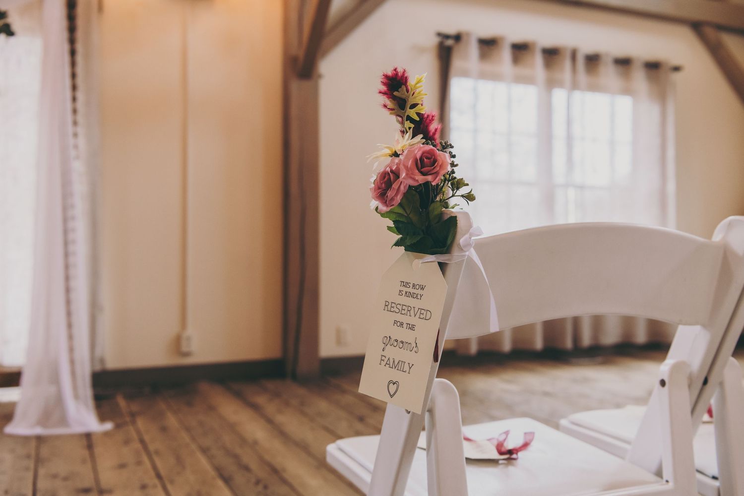 White curtains and decorative floral arrangements line an elegant indoor wedding ceremony venue.