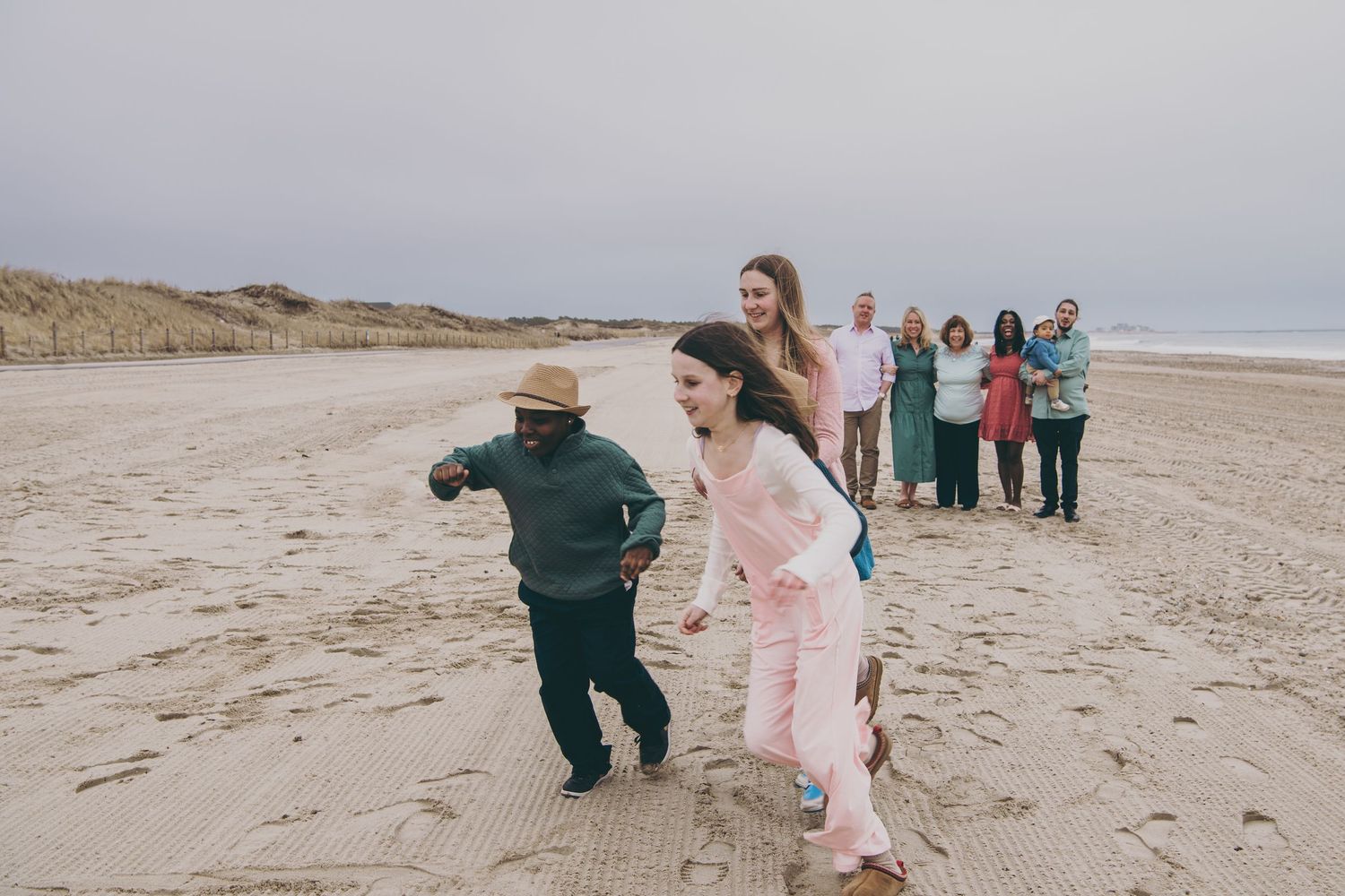 People enjoying a playful moment on a sandy beach with dunes in the background.