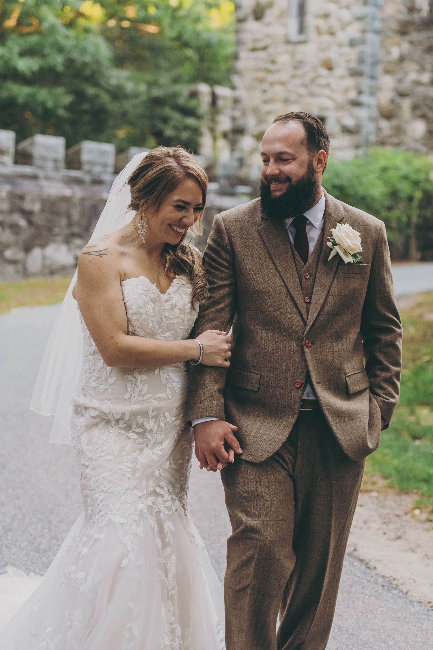 Happy couple walking together along stone wall path during wedding celebration.
